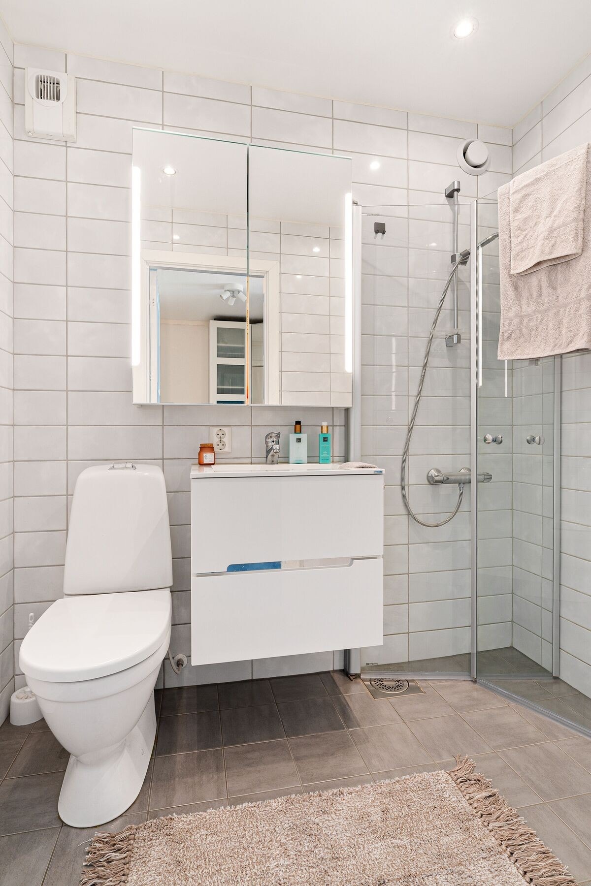 Badet er utstyrt med varme i gulv, innredning med servant, toalett, speilskap, praktiske innfellbare dusjdører og dusjgarnityr på vegg. Galleribilde