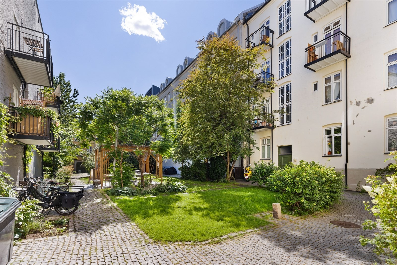 Idyllisk og pent opparbeidet bakgård med brostein, plen og beplantning. Galleribilde