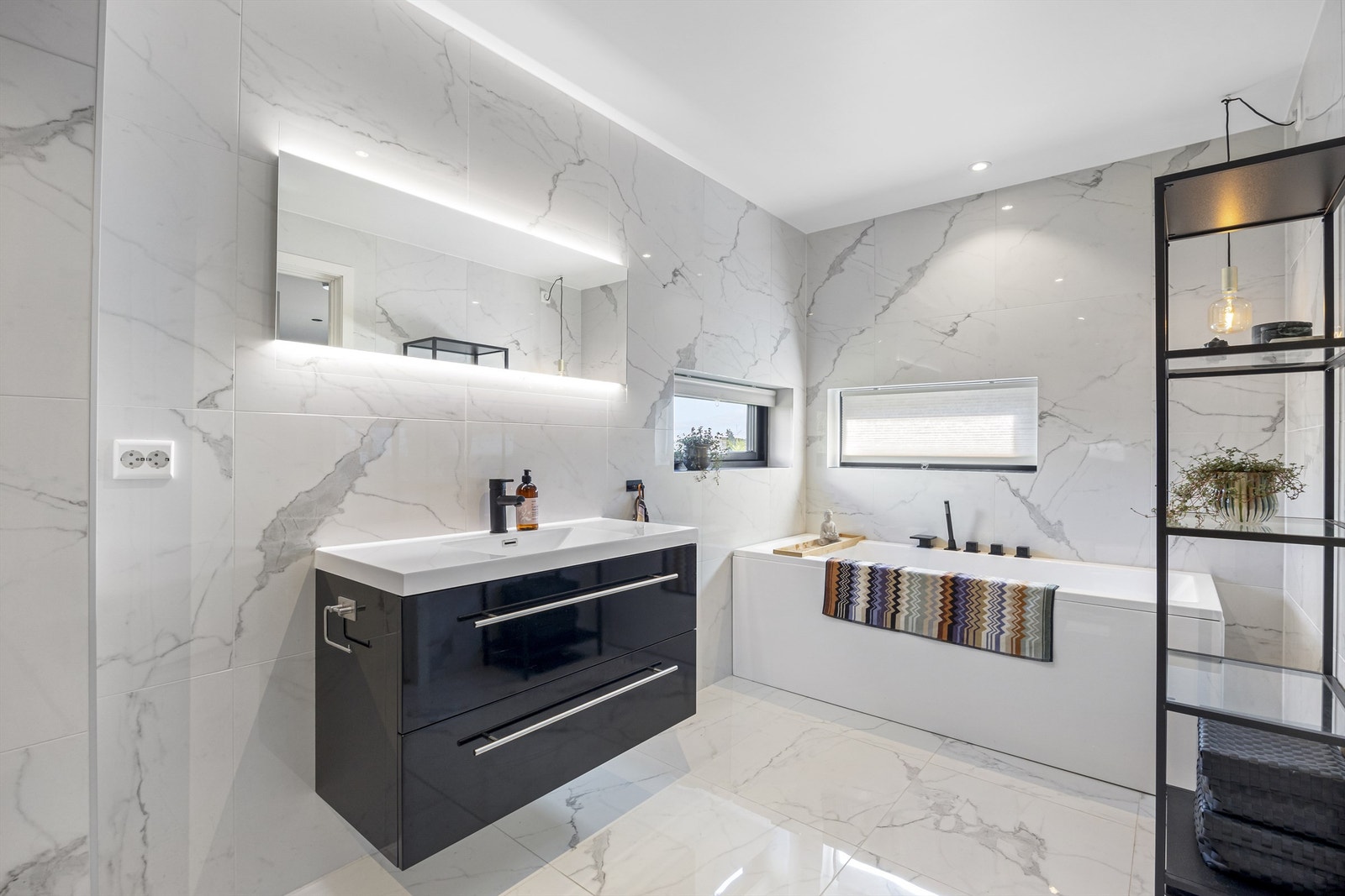 Pent flislagt bad med badekar, dusj, servantinnredning, toalett og speil med belysning Galleribilde