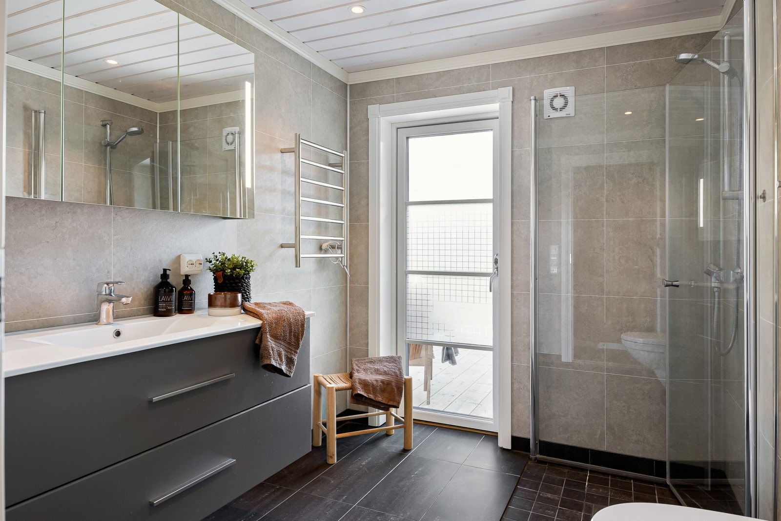 Flott og moderne bad på 5 kvm bestående av dusjnisje med innfellbare dusjdører som gir ekstra gulvplass når dusjen ikke brukes, innredning med skuffer og servat, speilskap med oppbevaringsplass og vegghengt WC Galleribilde