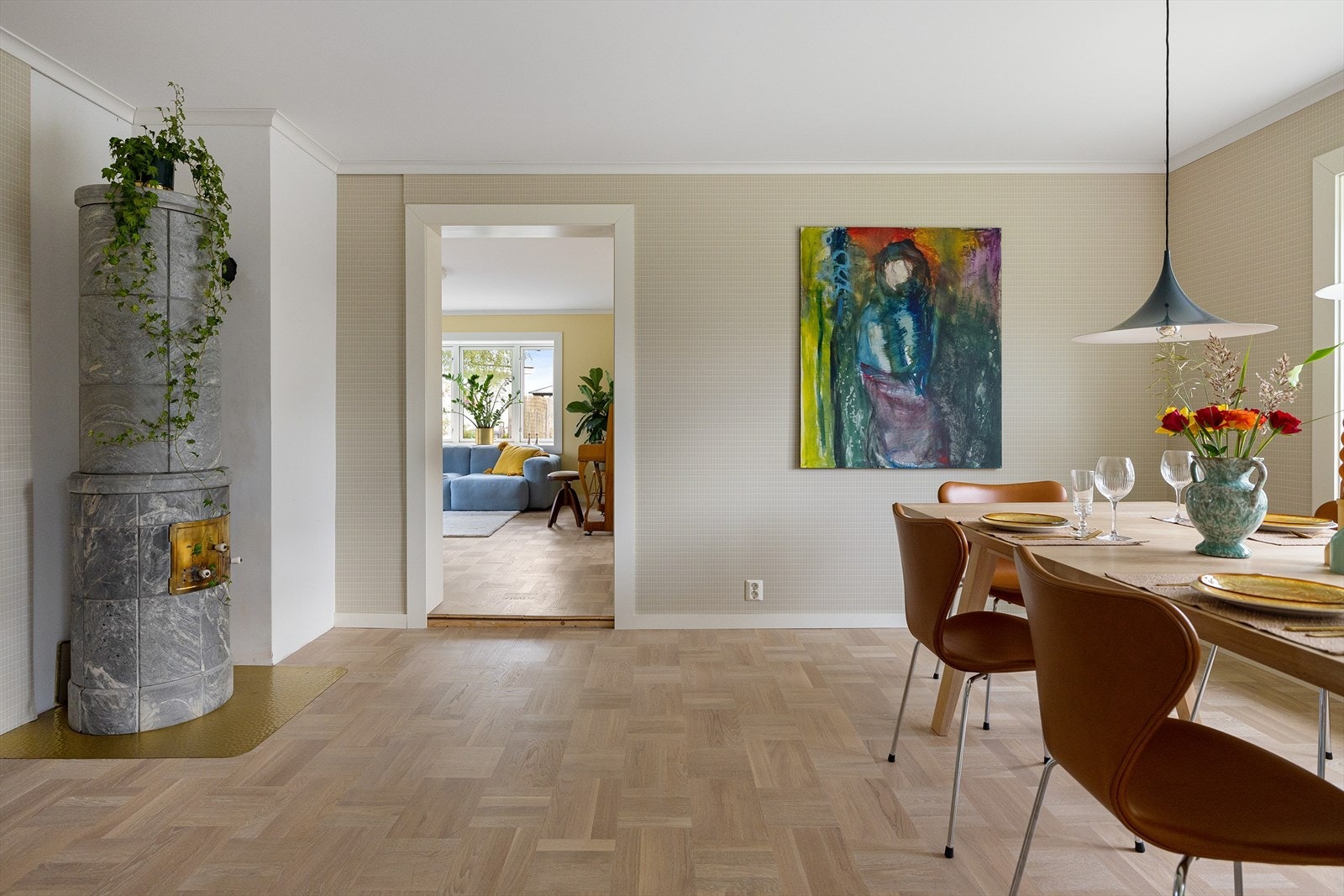 To stuer og kjøkken ligger halvåpent på rad etter hverandre. Her tegnes rommene opp i stramme linjer av hvit belistning og hvitt tak mot en elegant sandfarget rutemønstret tapet. Galleribilde