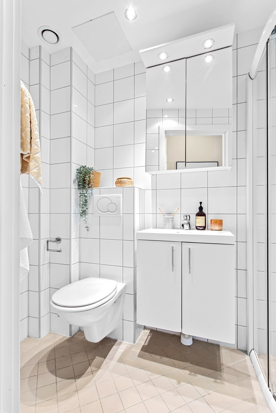 Delikat, flislagt bad med veggmontert wc, servant | skap med speilskap over, dusjhjørne og opplegg til vaskemaskin Galleribilde