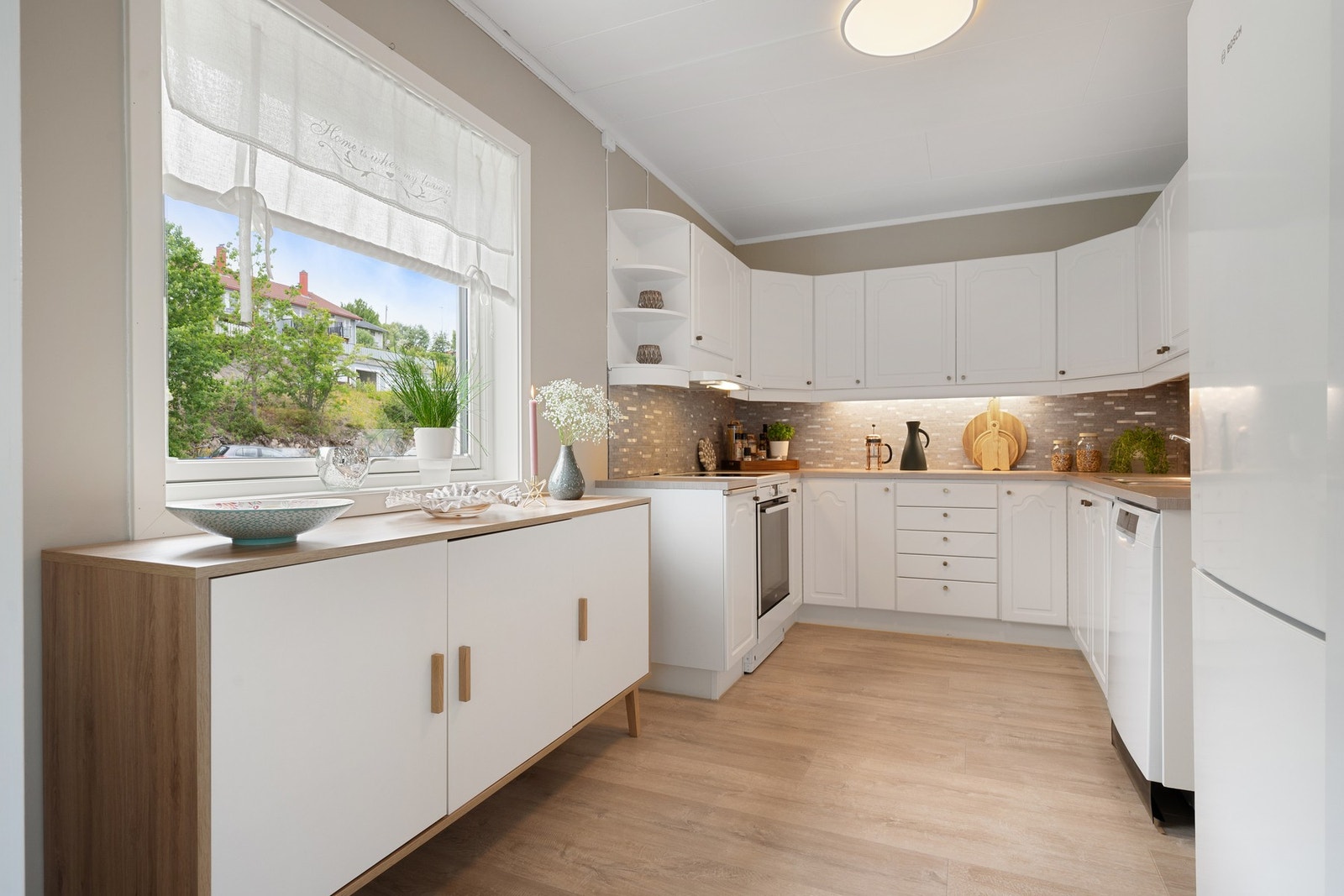 Kjøkkenet har en tidløs innredning med hvite, profilerte fronter og benkeplate av laminat Galleribilde