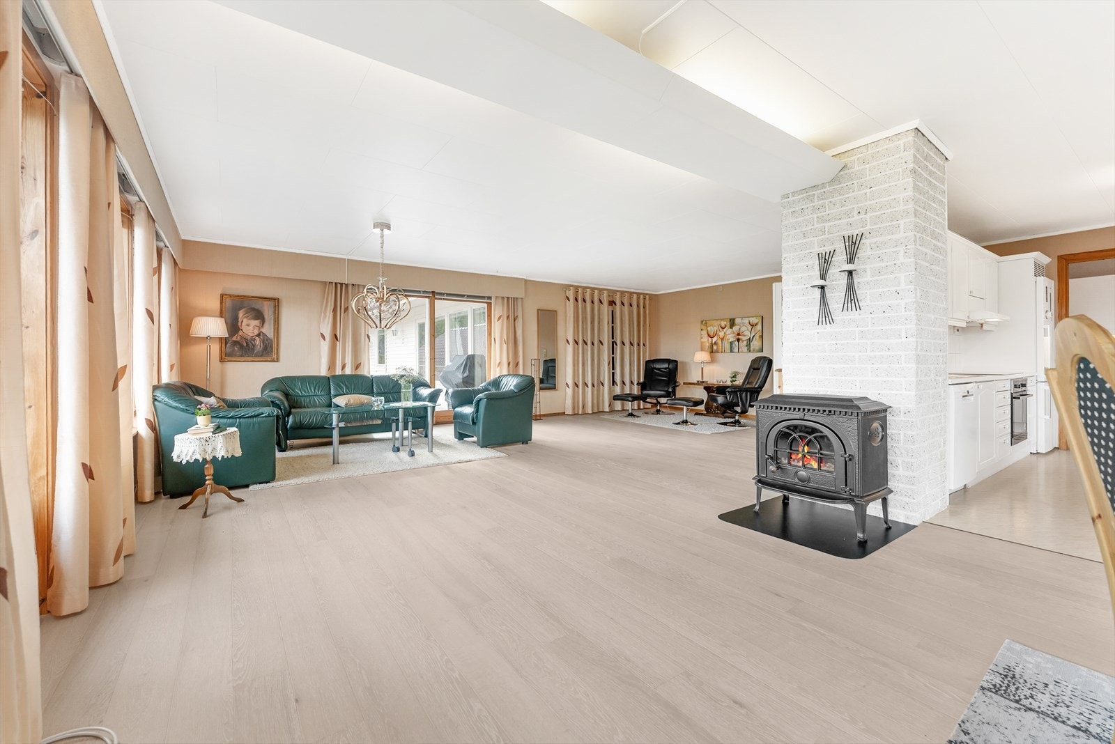 Stor og lys stue med vedovn. Kjøkken kan skimtast mot høgre Galleribilde