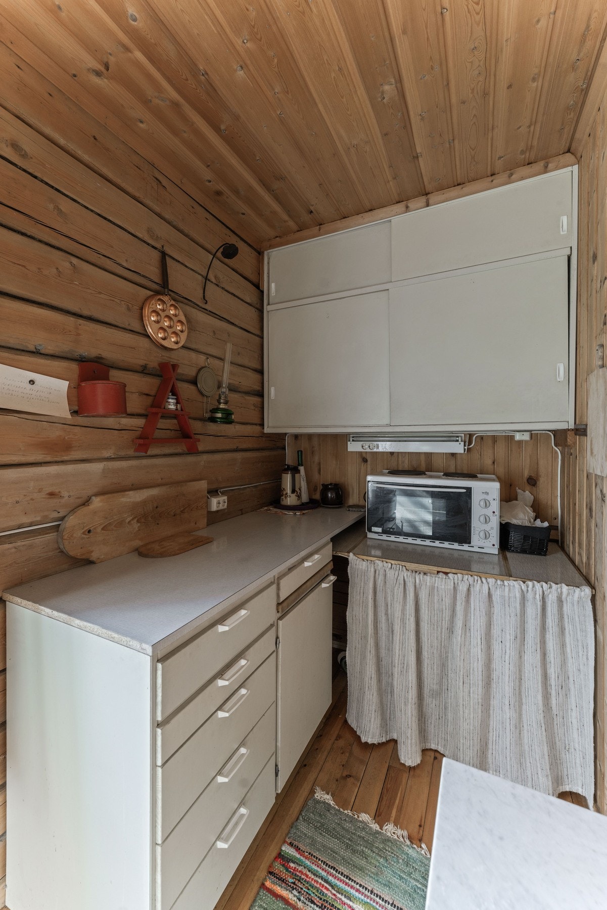 Kjøkkenet har plass til frittstående hybelkomfyr og kjøleskap, og er utstyrt med overskap og åpen oppbevaring med gardinløsning under benken. Galleribilde