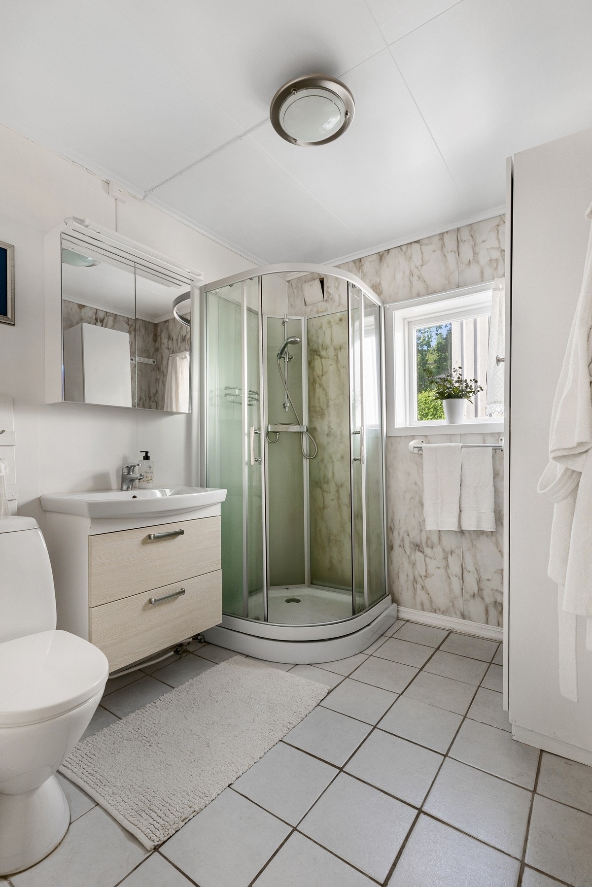 Baderommet består av servant med underskuffer, vegghengt speilskap, dusjkabinett og gulvstående toalett Galleribilde