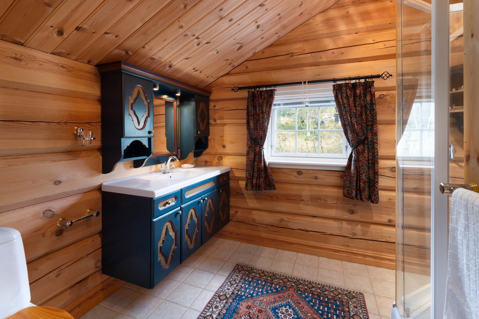 Andre etasje har også et romslig bad, utstyrt med både dusjkabinett og gulvstående vannklosett. Innredningen består av servant, unikt servantskap med flotte detaljer, speil og godt med lagringsplass. Badet har i likhet med soverommet mønet himling. Galleribilde