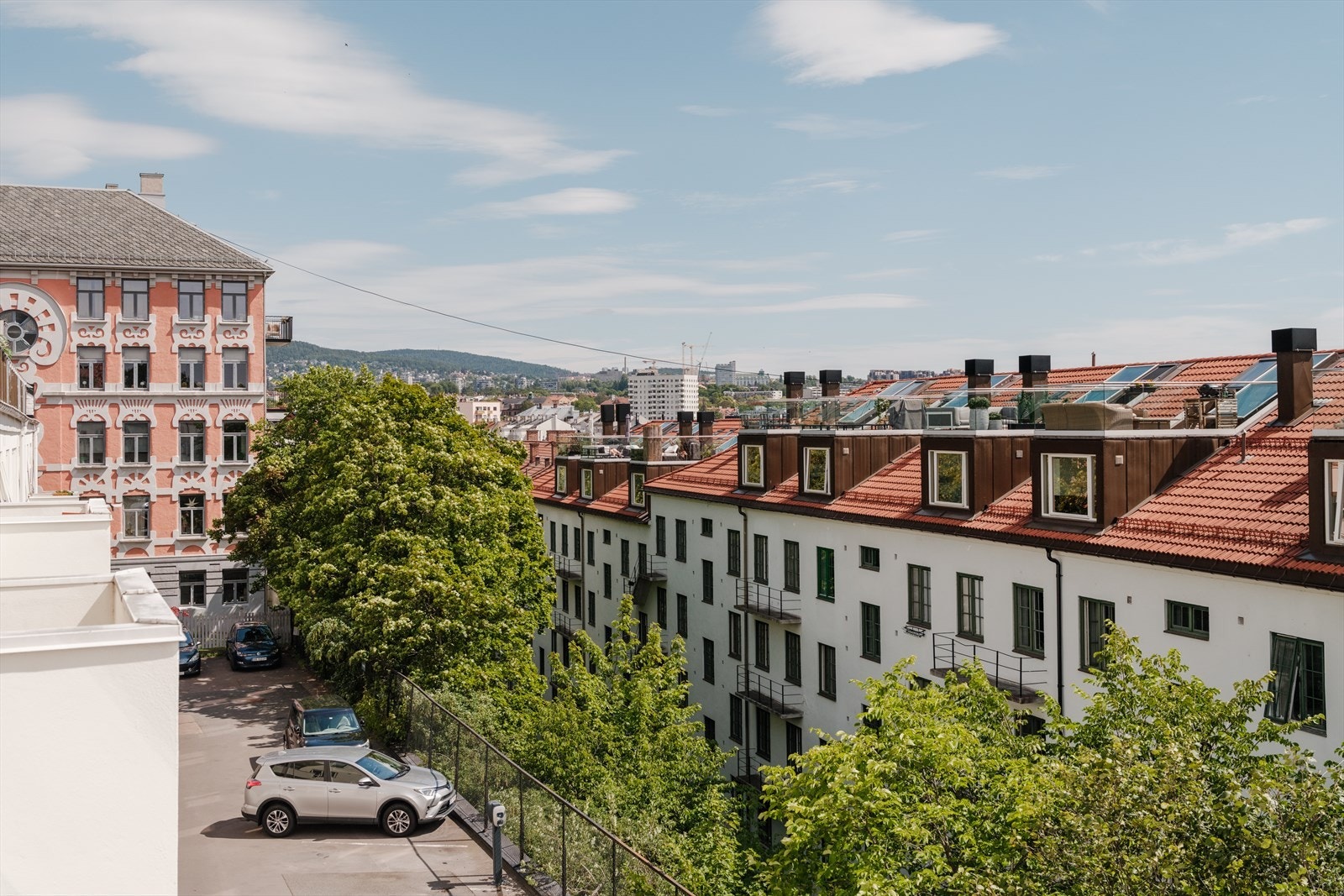 Utsikten vender mot klassiske bygårder med karakteristiske teglsteinstak og grønne trær som gir et frodig preg. Galleribilde