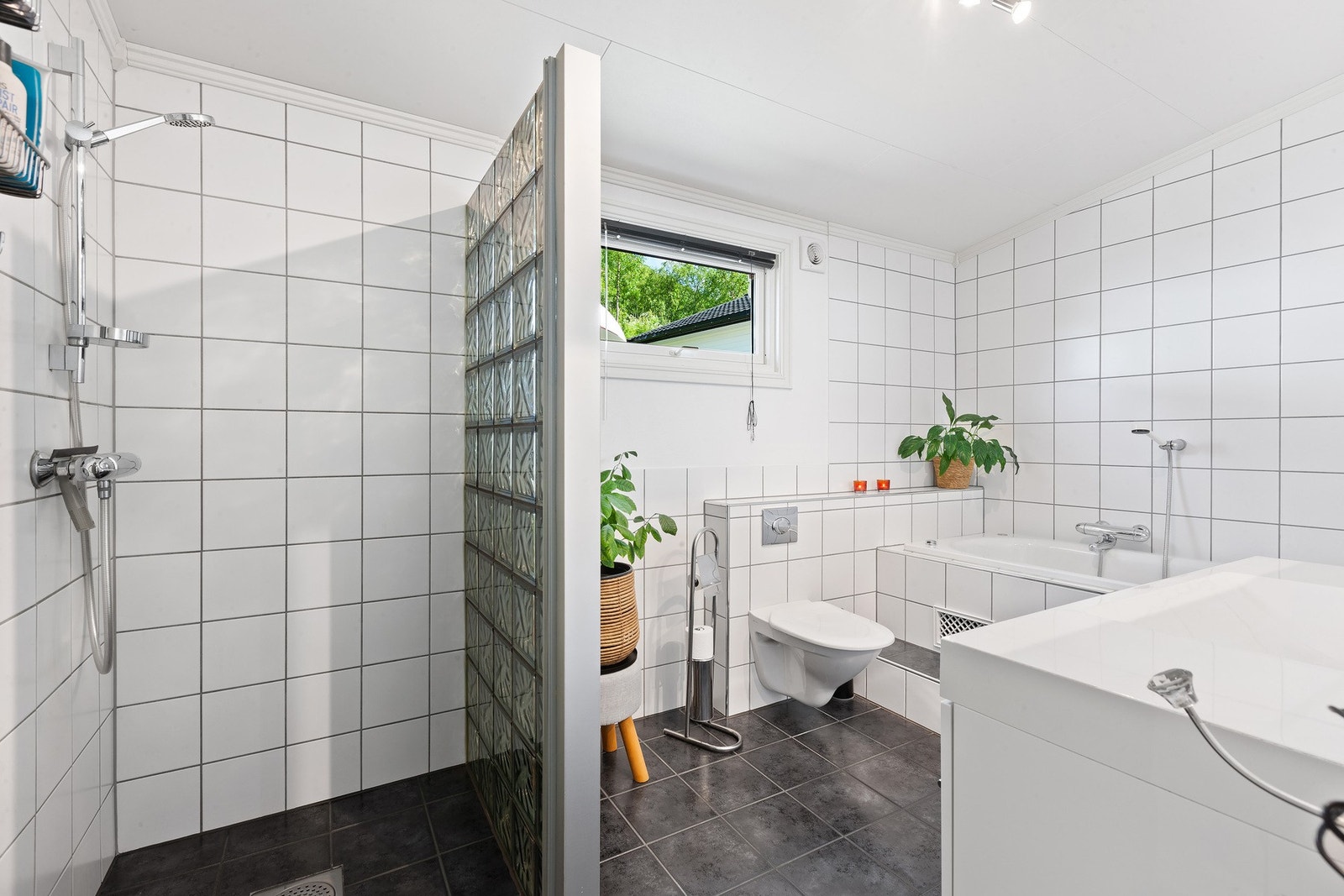 Lyst bad med servant, vegghengt toalett, dusjnisje og badekar. Galleribilde