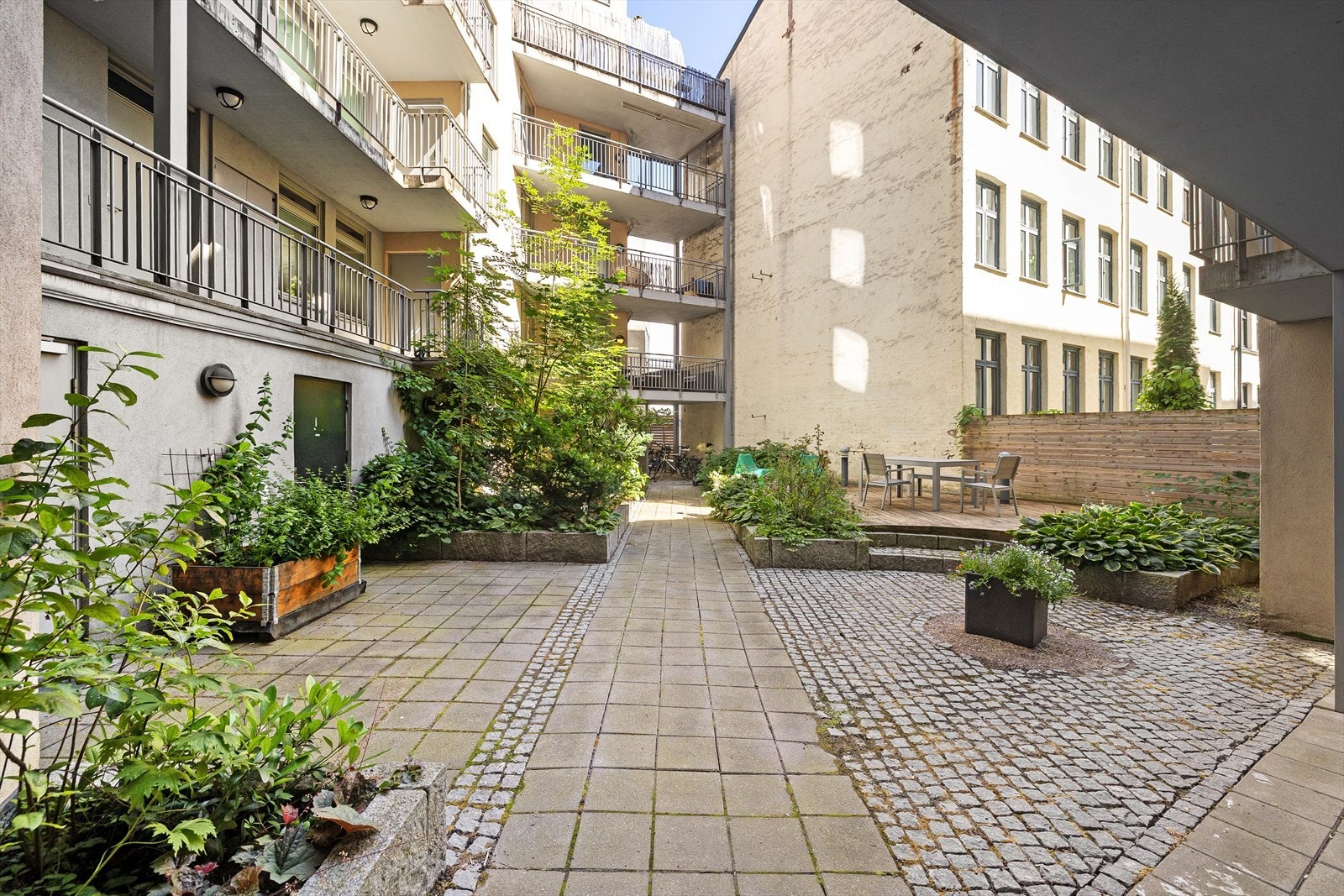 Hyggelig, brosteinsbelagt bakgård med sittegrupper og beplanting. Galleribilde