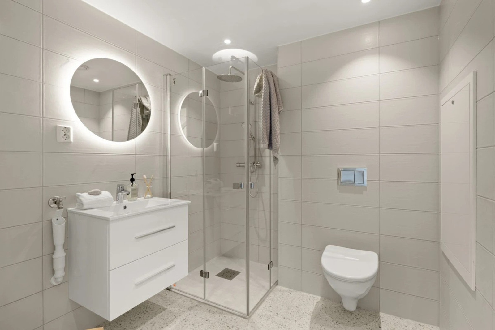 Her får du et lekkert og gjennomført bad med italienske fliser og moderne detaljer. Badet er innredet med dusj med dusjarmatur på vegg og svingbare dusjdører i glass, veggmontert klosett og moderne baderomsinnredning med servant Galleribilde