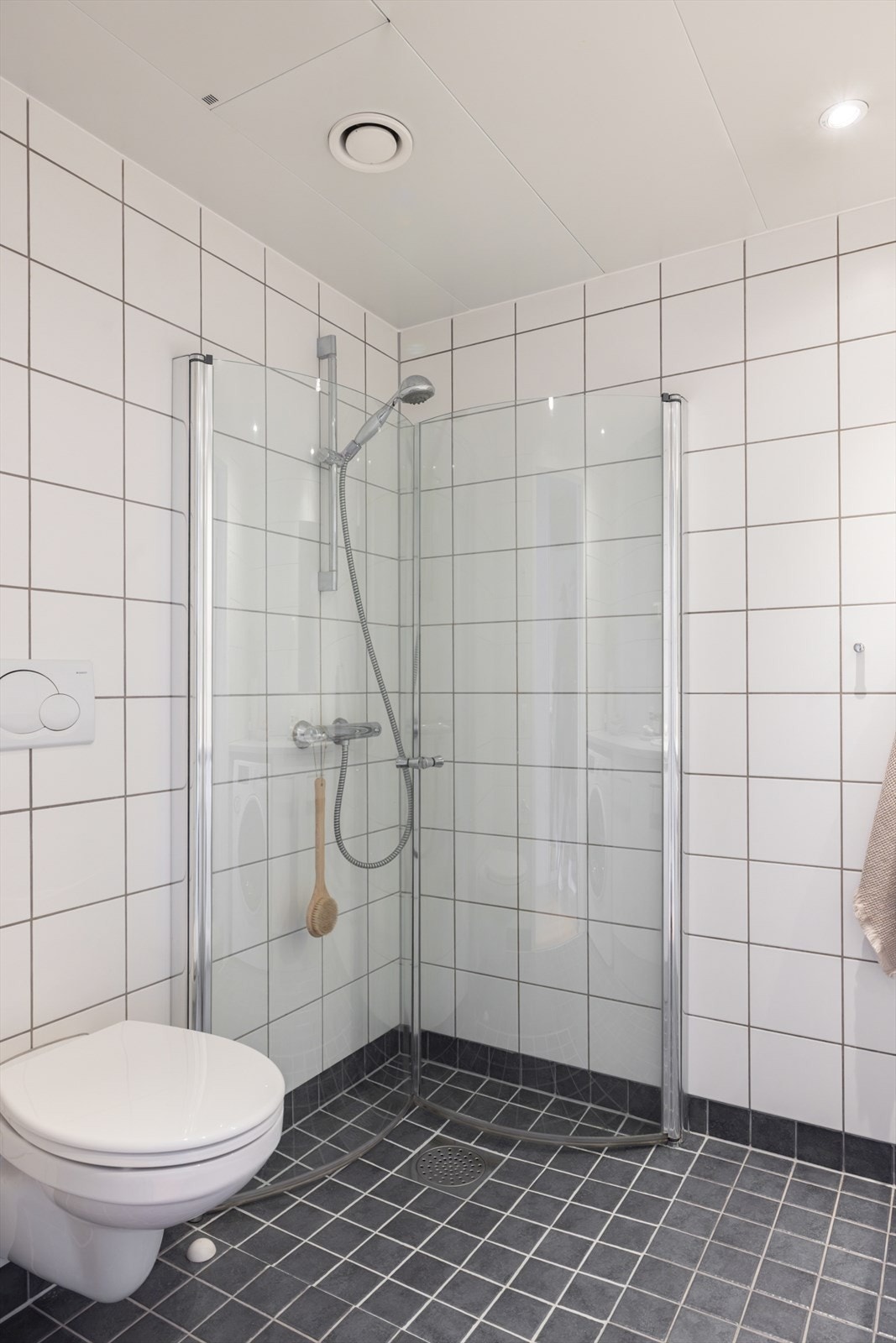 Badet inneholder en dusjnisje med svingbare dører, vegghengt toalett, og opplegg for vaskemaskin. Galleribilde