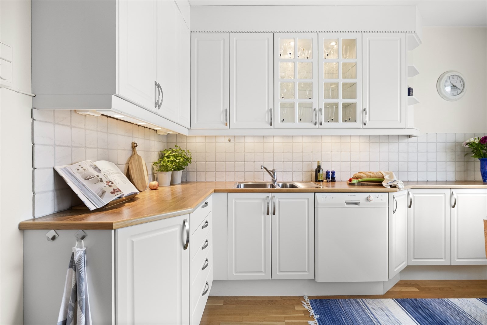 Innredningen har hvite, profilerte fronter, vitrineskap og benkeplater i laminert eik. Kjøkkenet er utstyrt med planlimt rennebeslag, oppvask- og skyllekum samt ettgreps kjøkkenarmatur. Galleribilde