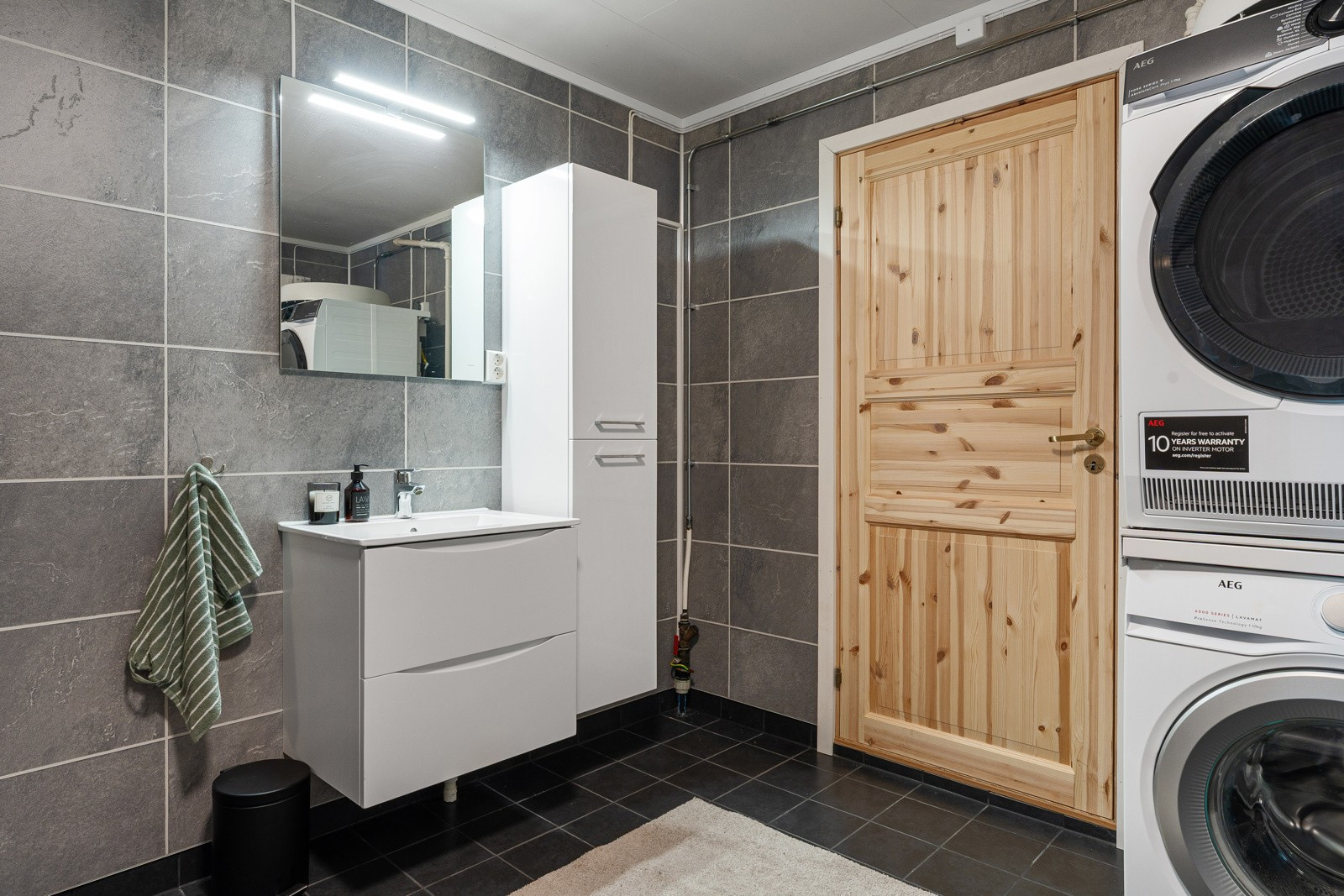 Badet har fliser på gulv, gulvvarme, dusjkabinett og opplegg for vaskemaskin. Det er dør med adkomst til garasje.