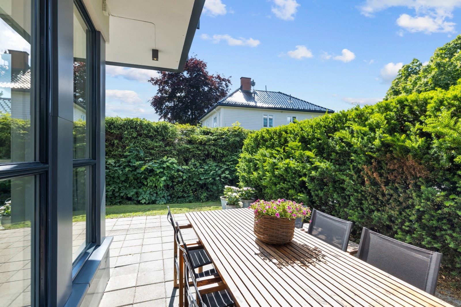 Hyggelig uteplass med bord, stoler og frodig hekk - perfekt for rolige sommerdager. Galleribilde