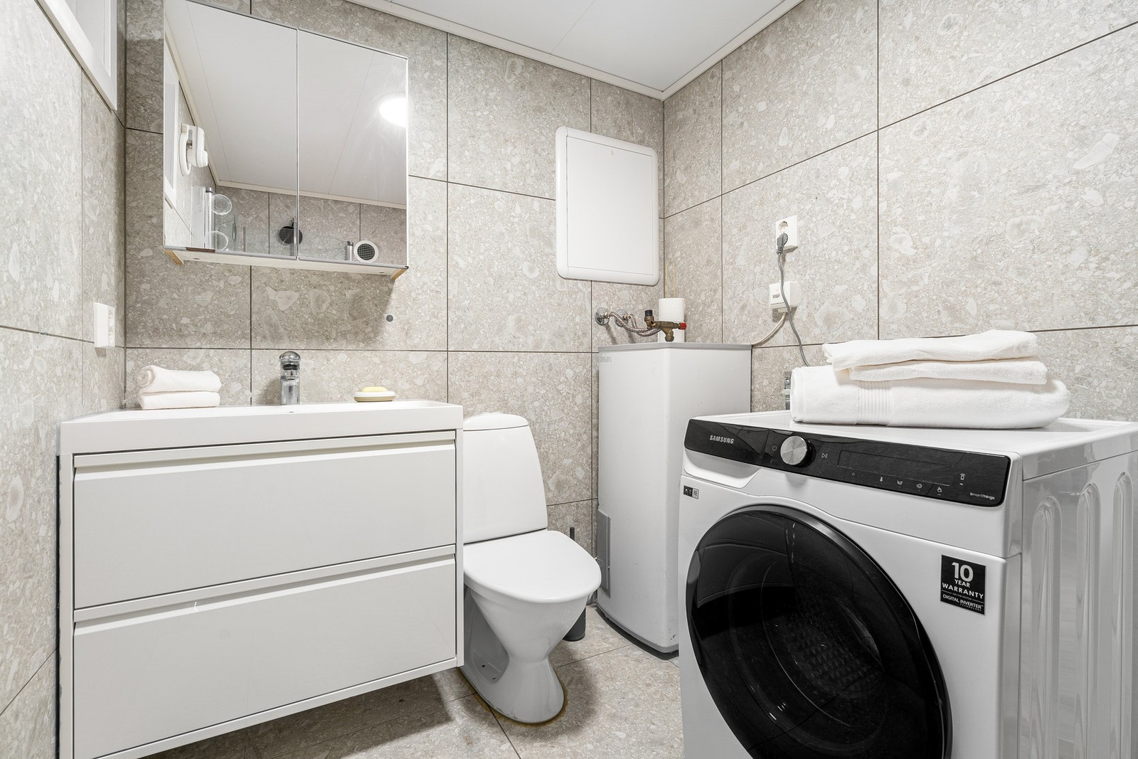 Badet er utstyrt med opplegg for vaskemaskin, varmtvannsbereder og dusjhjørne med innfellbare dører. Galleribilde