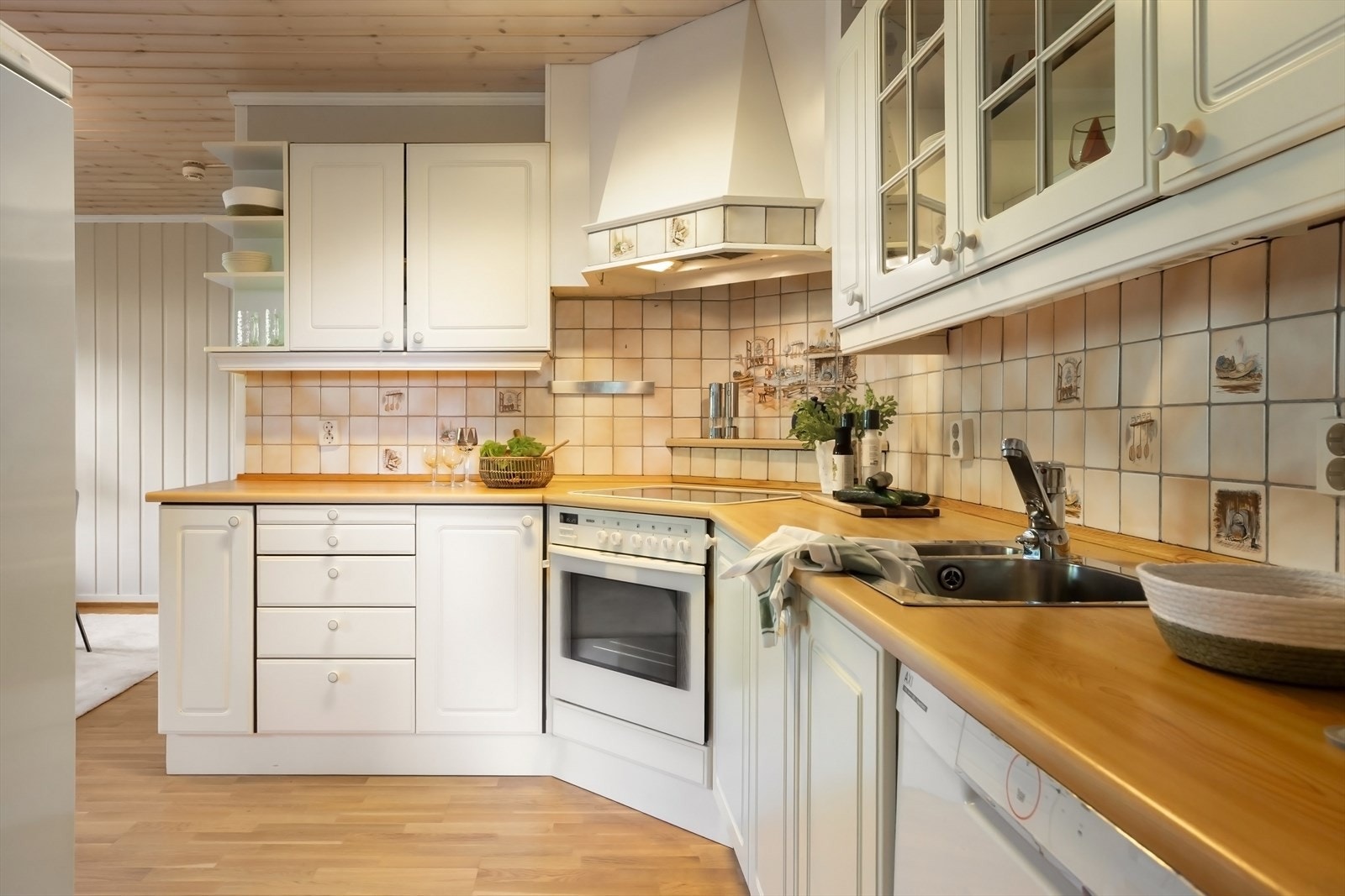 Kjøkkeninnredning med profilerte fronter. Lyslister og belysning under overskap. Fliser på vegg over benkeskap. Laminat benkeplate med nedfelt kum i rustfritt stål. Galleribilde