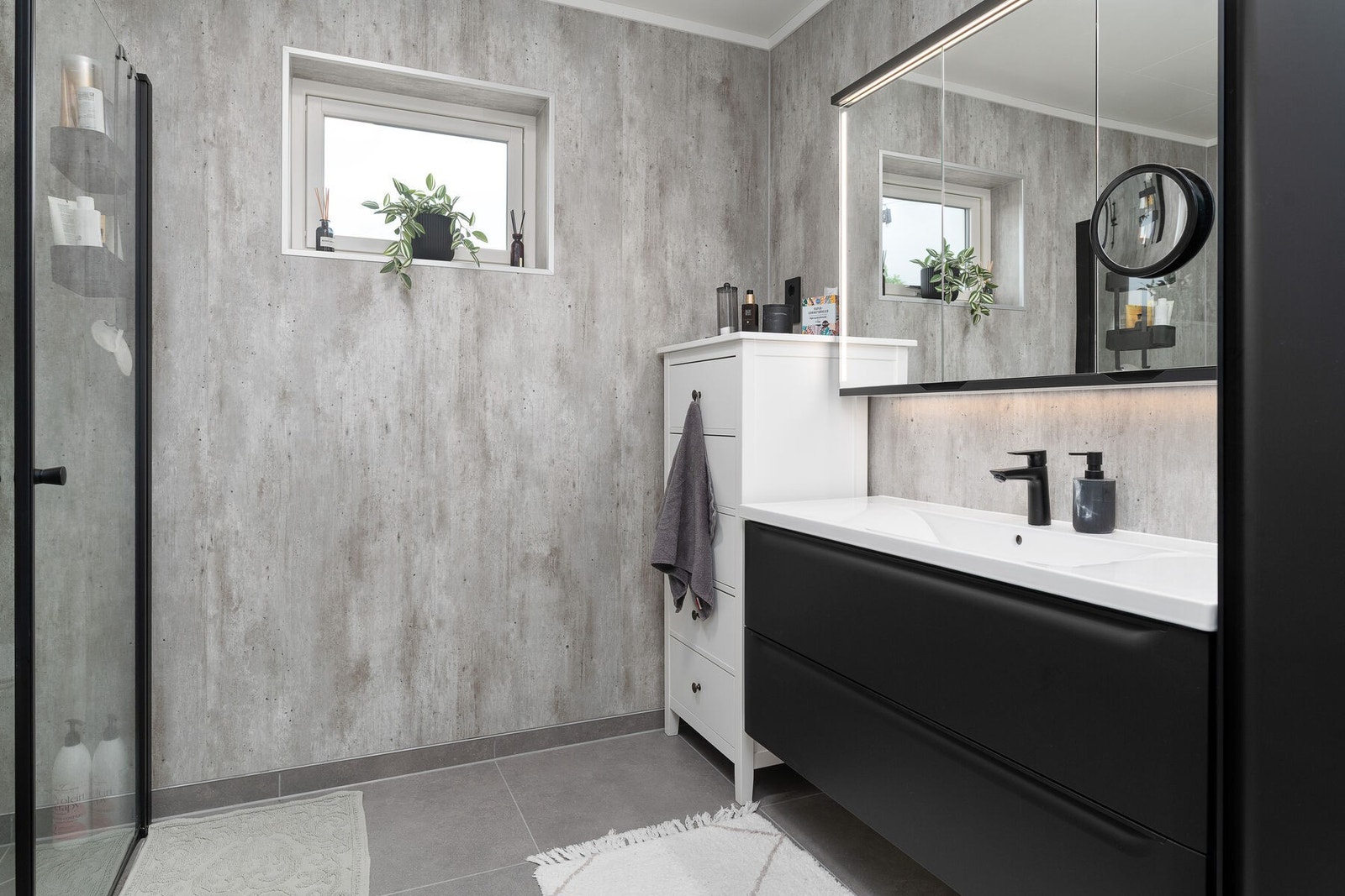 Moderne bad med servant på skuffeseksjon, speilskap med lys, vegghengt toalett og dusjhjørne. Galleribilde