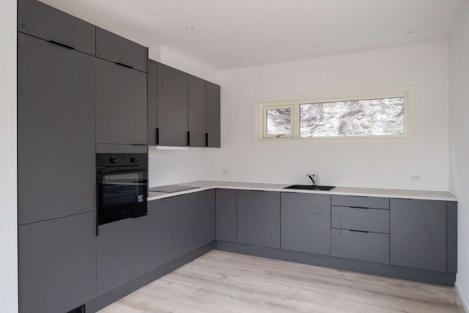 Stilfullt mørkt kjøkken med integrerte hvitevarer som kjøleskap, fryser, stekeovn, induksjonstopp og oppvaskmaskin. Galleribilde