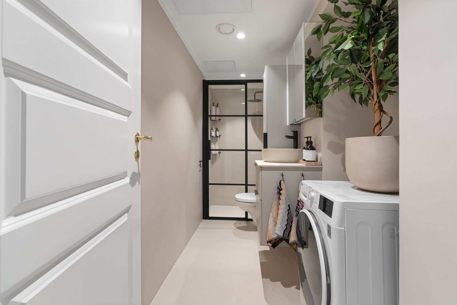 Delikat bad pusset opp i 2023 med lyse overflater, downlights i himling og opplegg for vaskemaskin og tørketrommel. Galleribilde