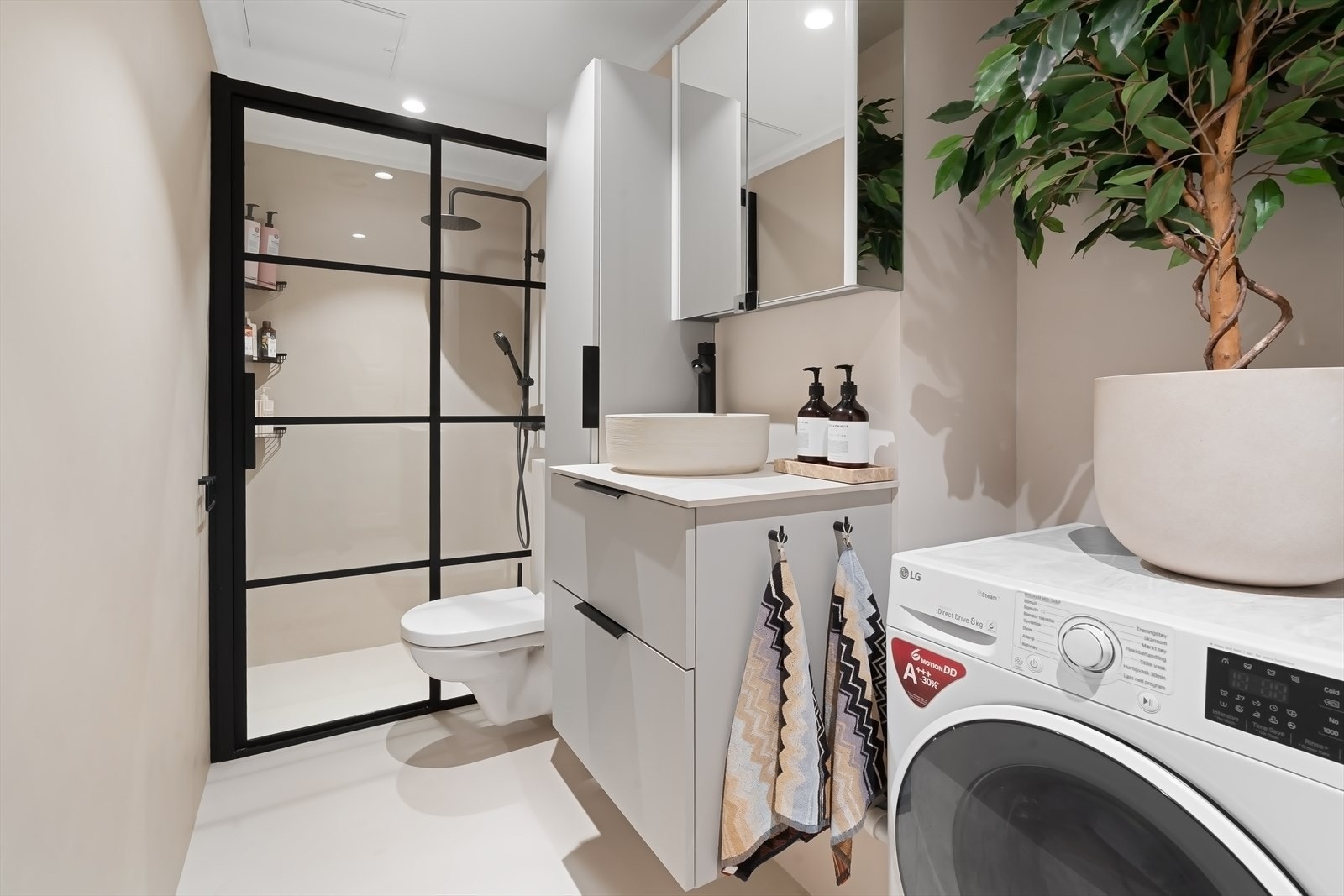 Innredet med høyskap, servant med skuffer, speilskap, veggmontert toalett og egen dusjnisje. Galleribilde