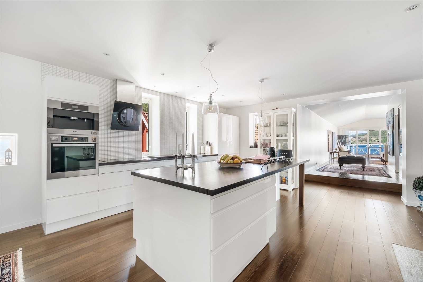 Velutstyrt kjøkken i tidløs hvit stil, med integrerte hvitevarer og kjøkkenøy som kombinerer form og funksjon. Galleribilde