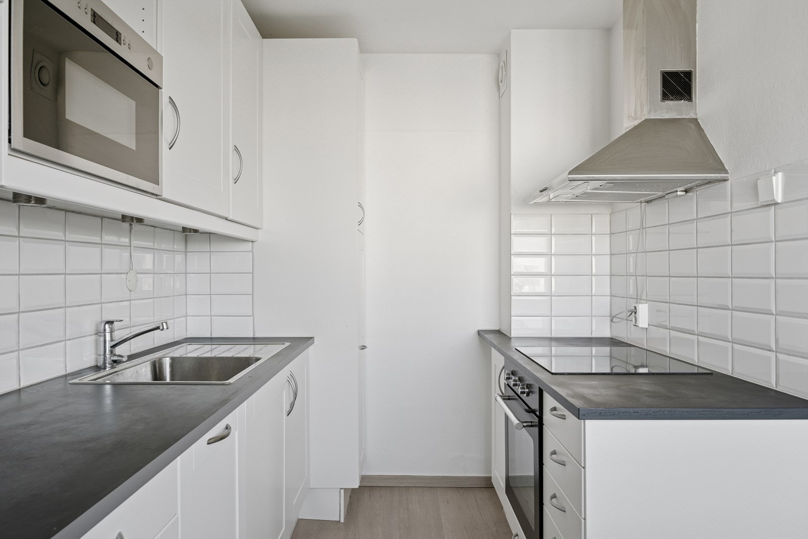 Kjøkkenet har glatte, hvite delvis profilerte fronter og laminat benkeplate med nedfelt stålkum og rillefelt, samt ettgreps kjøkkenkran. Ventilator med kullfilter. Galleribilde