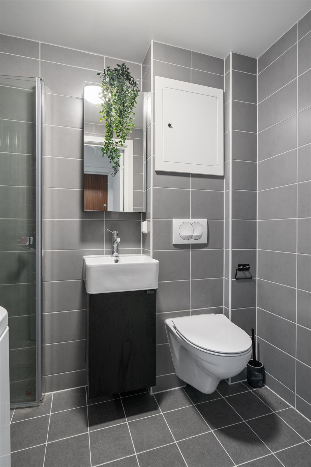 Vegghengt toalett med skjult sisterne gir en strømlinjeformet finish, og dusjsonen har svingbare glassdører som utnytter plassen effektivt. Galleribilde