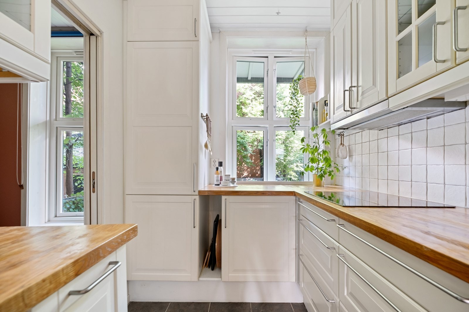 Pent kjøkken med innredning av klassiske, lyse fronter og en heltre benkeplate. Galleribilde