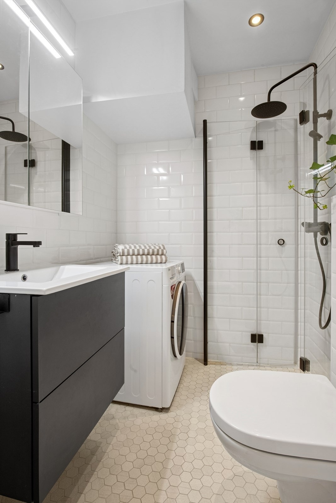 Badet inneholder vegghengt toalett, dusj med dusjhjørner, servant med ett-greps blandebatteri, servantskap, samt opplegg for vaskemaskin Galleribilde