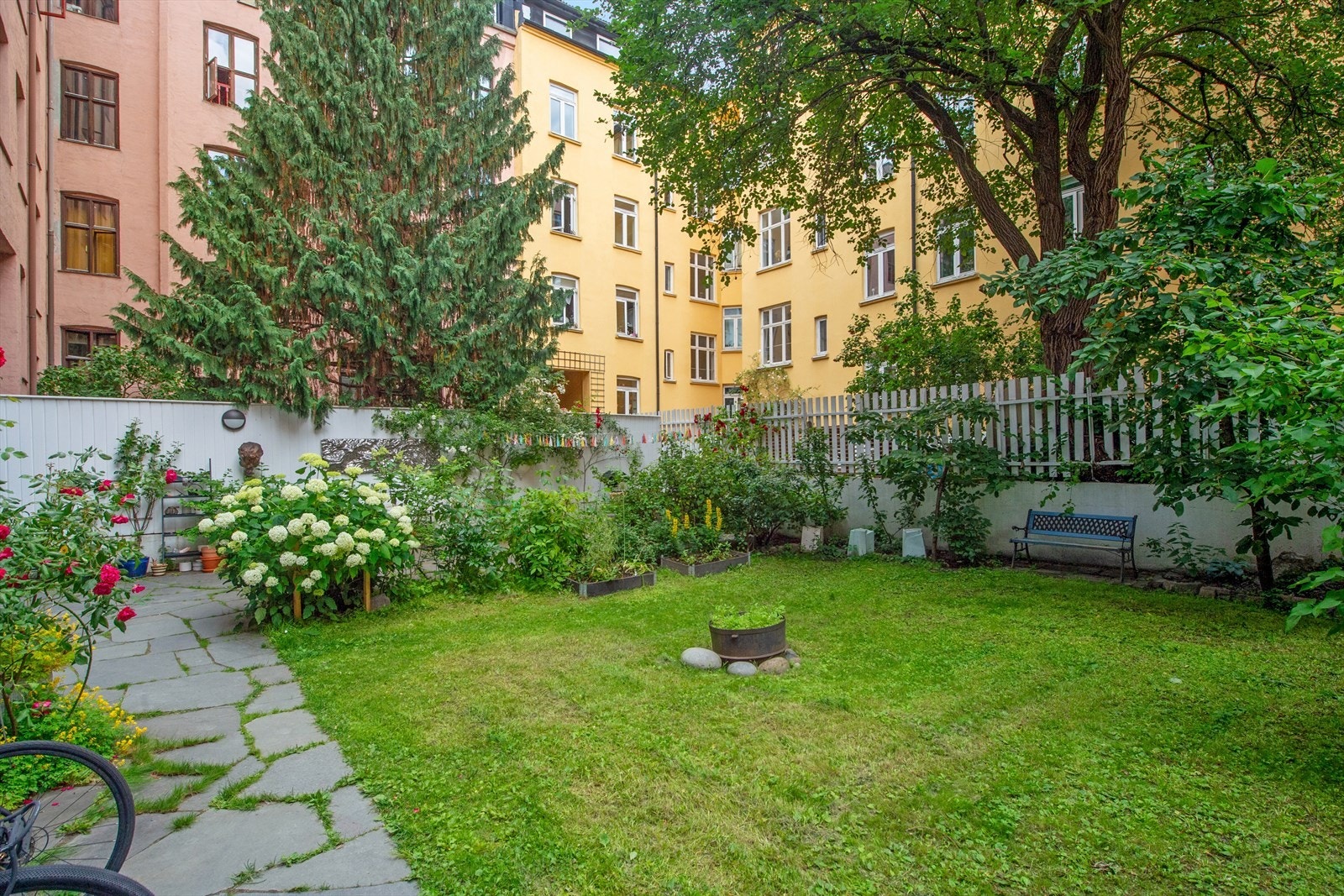 Grønn og frodig bakgård med hyggelige sittegrupper, blomstrende beplantning og god atmosfære - et skjermet og sosialt uterom midt i byen Galleribilde