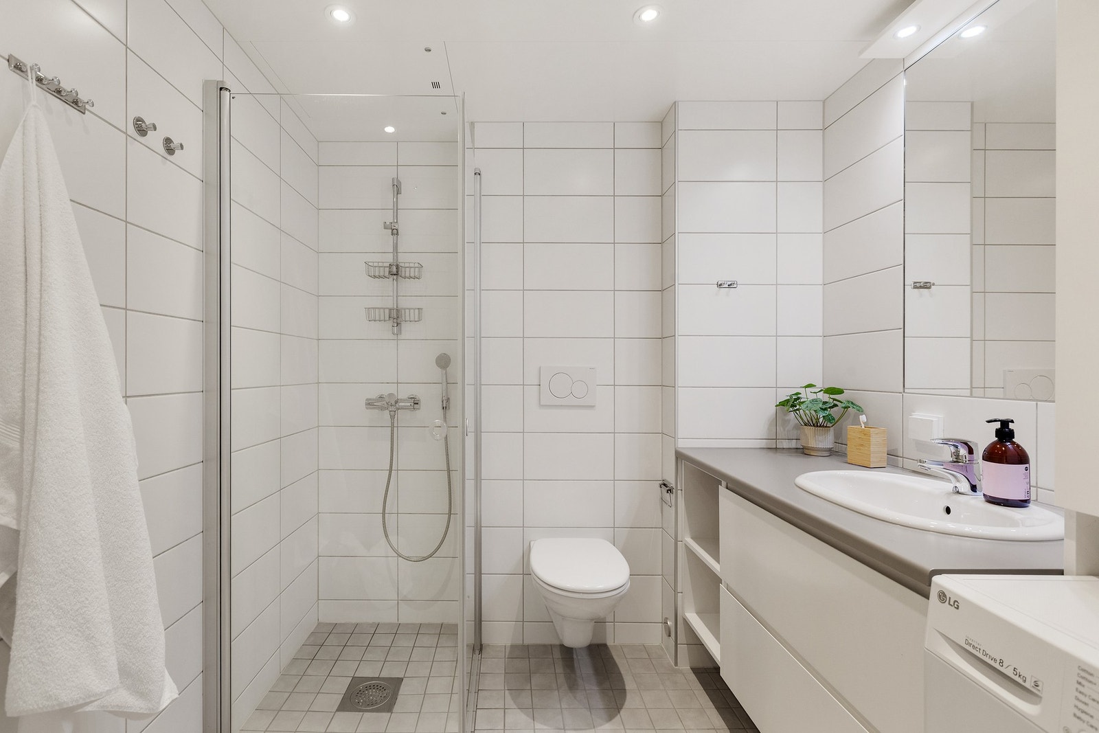 Badet er stort og har moderne innredning med vegghengt toalett, innfellbare dusjdører, speil og opplegg for vaskemaskin. Galleribilde