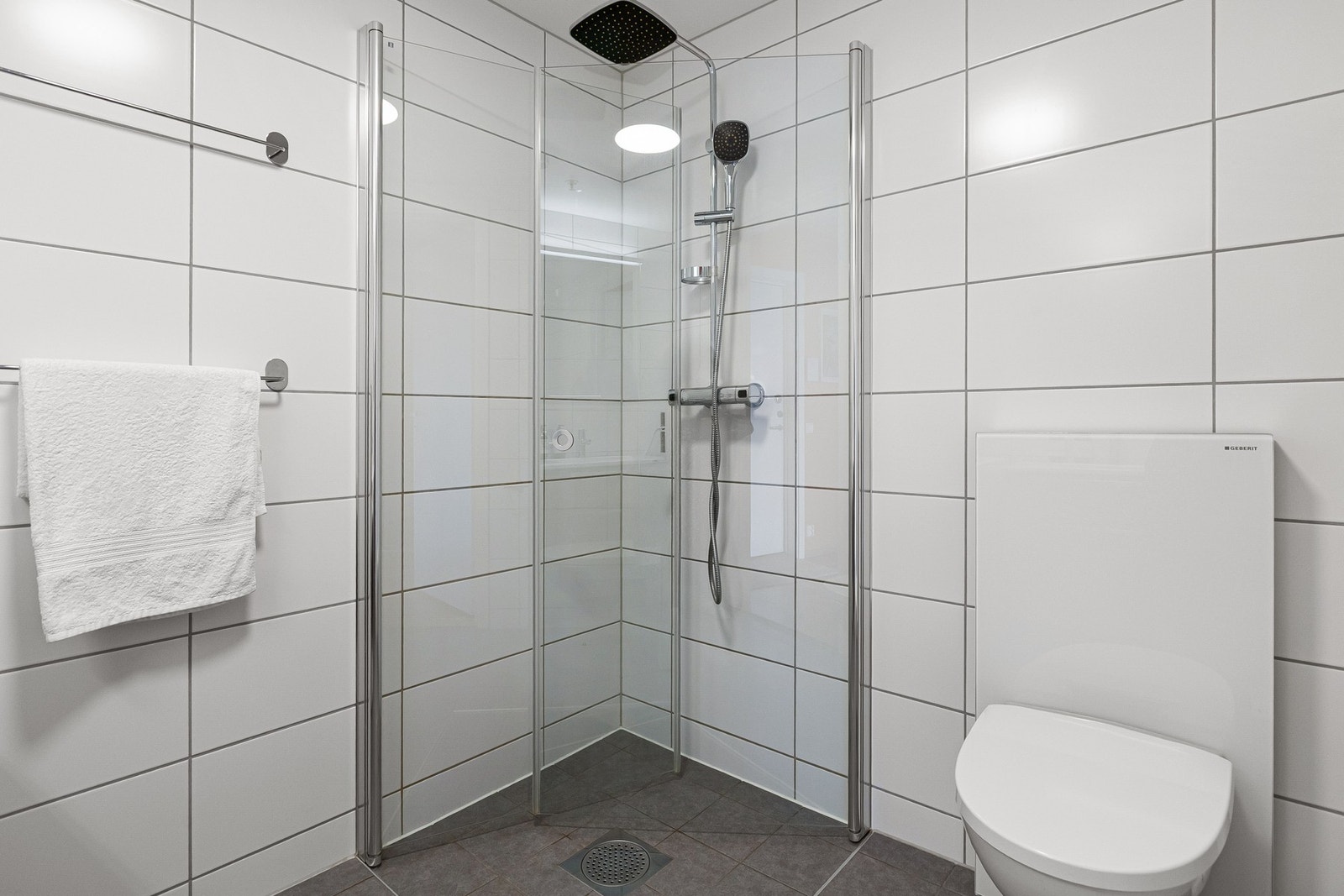 Baderommet inneholder servantskap med glatte fronter, heldekkende servant, veggmontert klosett, samt dusjhjørne med svingdører av herdet glass, sluk, blandebatteri, regnfallsdusj og hånddusj. Galleribilde