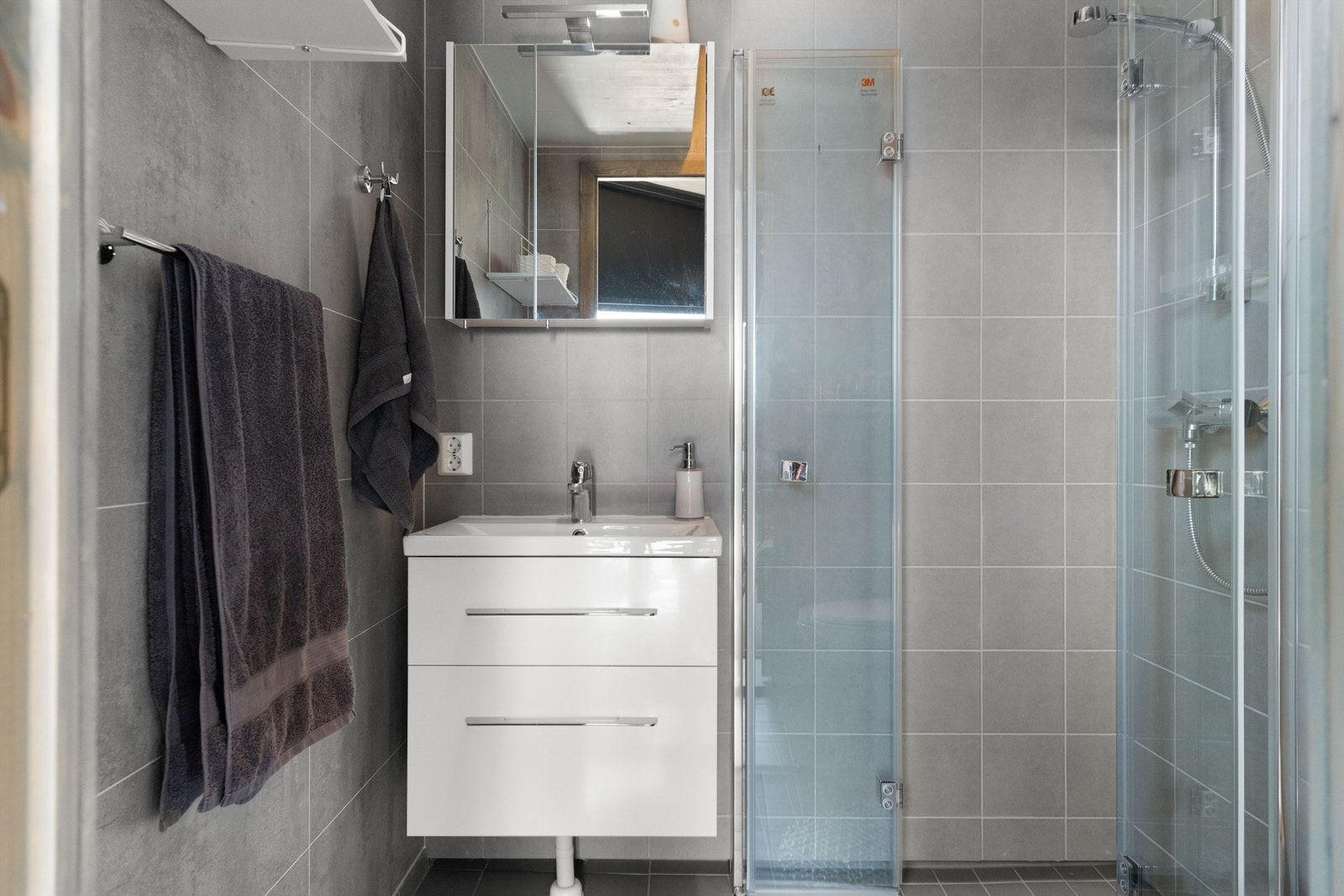 Badet har vegghengt dusjdør og toalett. Det er også innredning med glatte fronter, helstøpt servant, skuffeseksjon med myk lukking og speil med belysning. Galleribilde