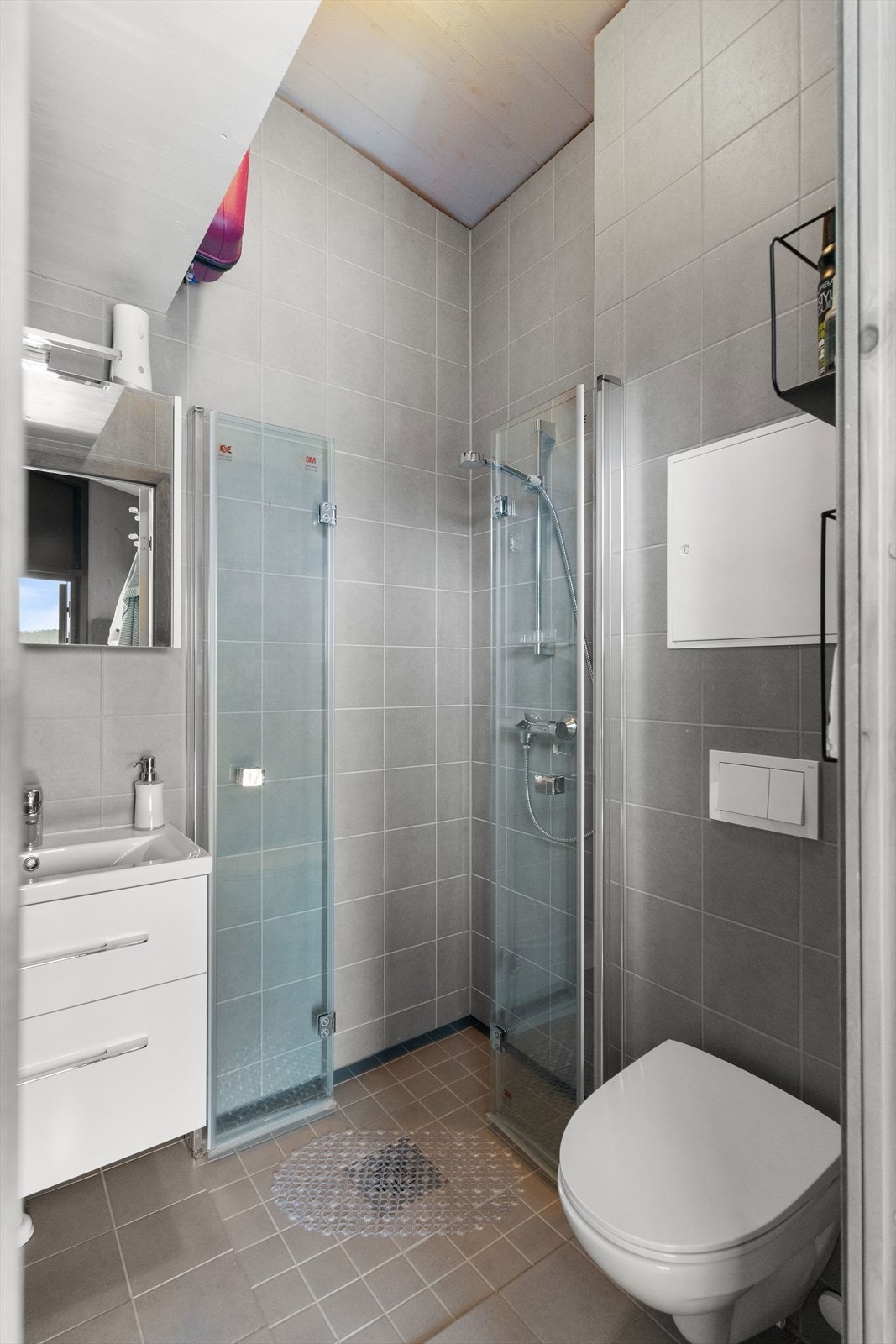 Det flislagte badet er elegant med delikate gråtoner. Store fliser dekker både vegger og gulv, mens dusjsonen har mindre fliser. Galleribilde