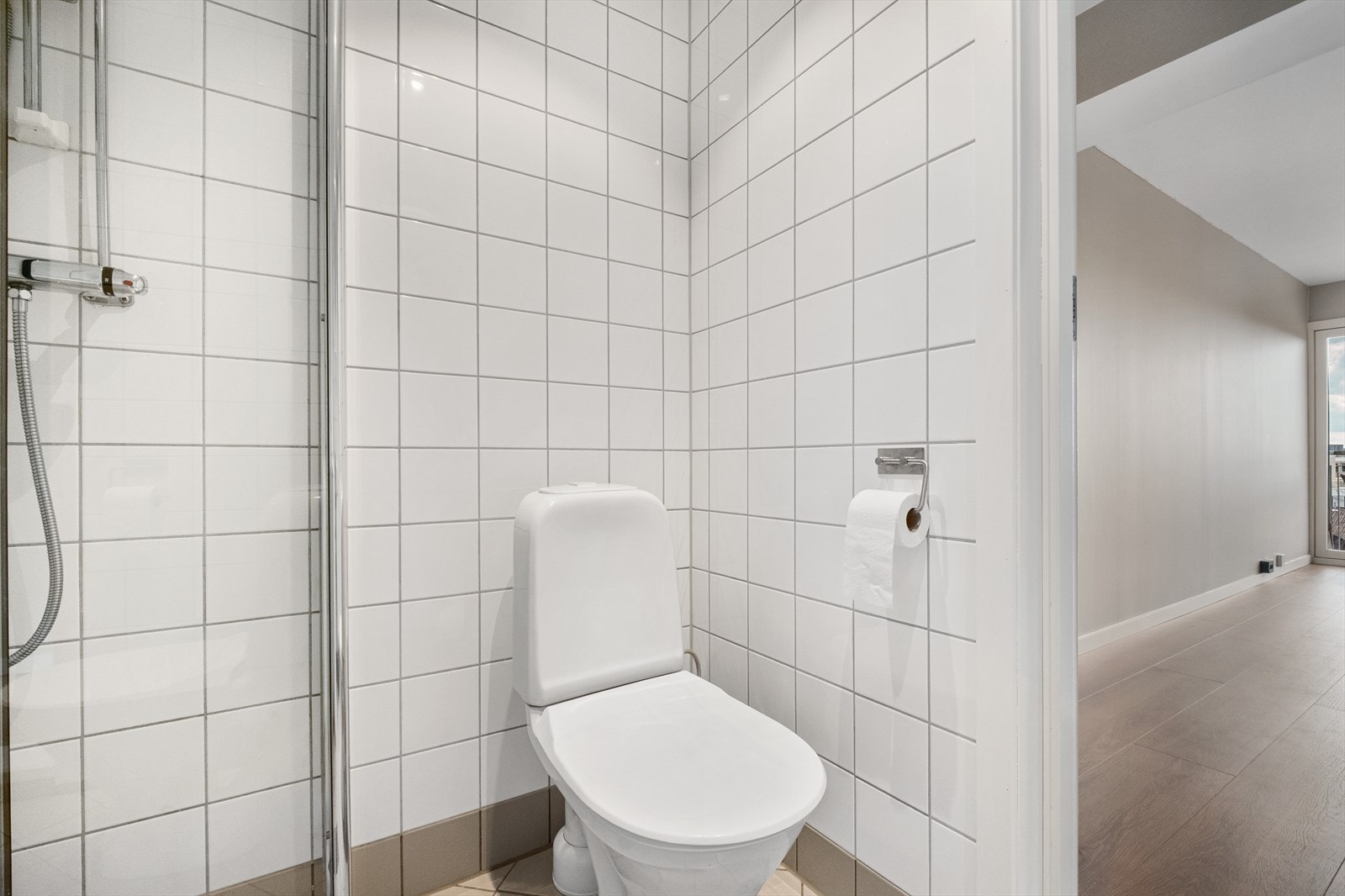 Badet er innredet med gulvstående klosett, baderomsinnredning med heldekkende servant, speil med lys og dusjvegger. Galleribilde