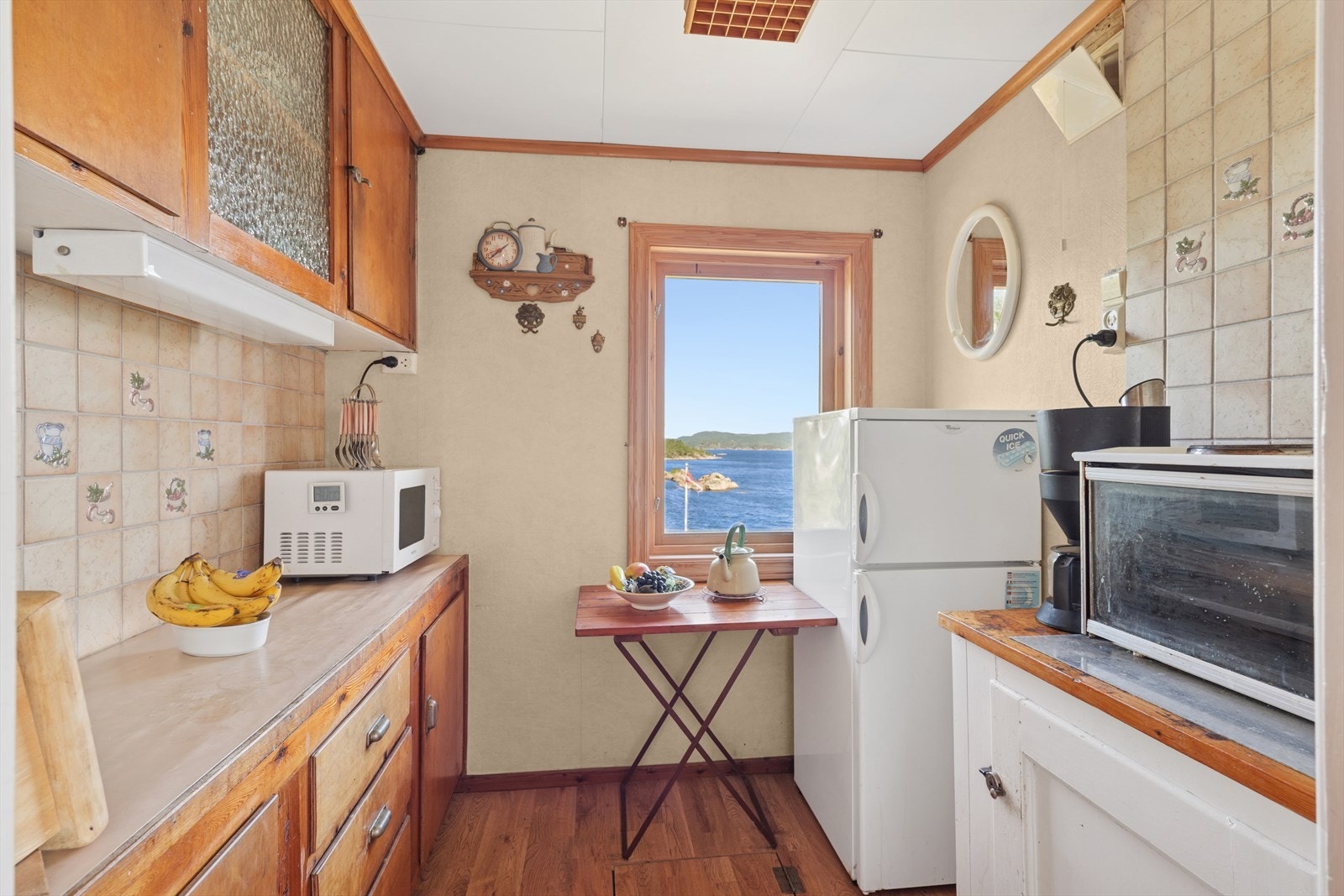 Koselig kjøkken med slette fronter og benkeplate i heltre. Kjøkkenet er utstyrt med frittstående kjøleskap, microovn og hybelkomfyr med avtrekksvifte over. Galleribilde