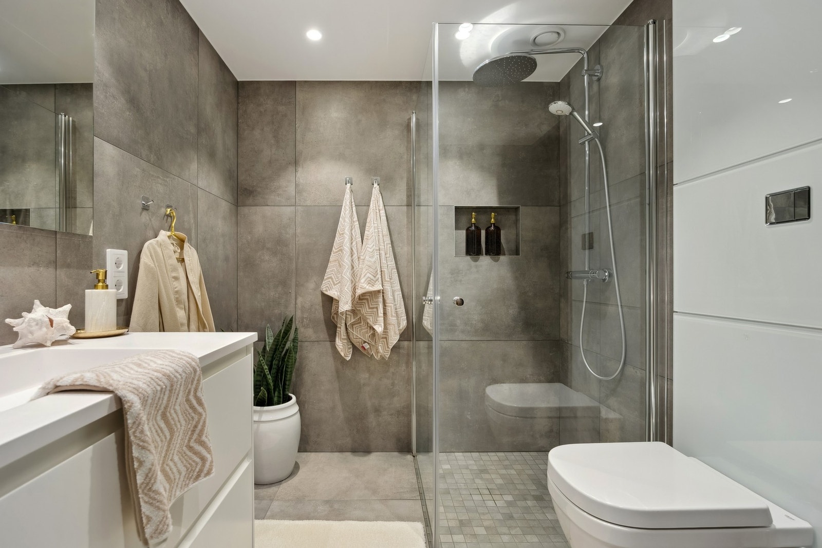 Badet er utstyrt med et romslig dusjhjørne med glassvegger som gir både funksjonalitet og en følelse av åpenhet, vegghengt toalett og servantinnredning med skuffer bidrar til et ryddig og praktisk miljø. Galleribilde