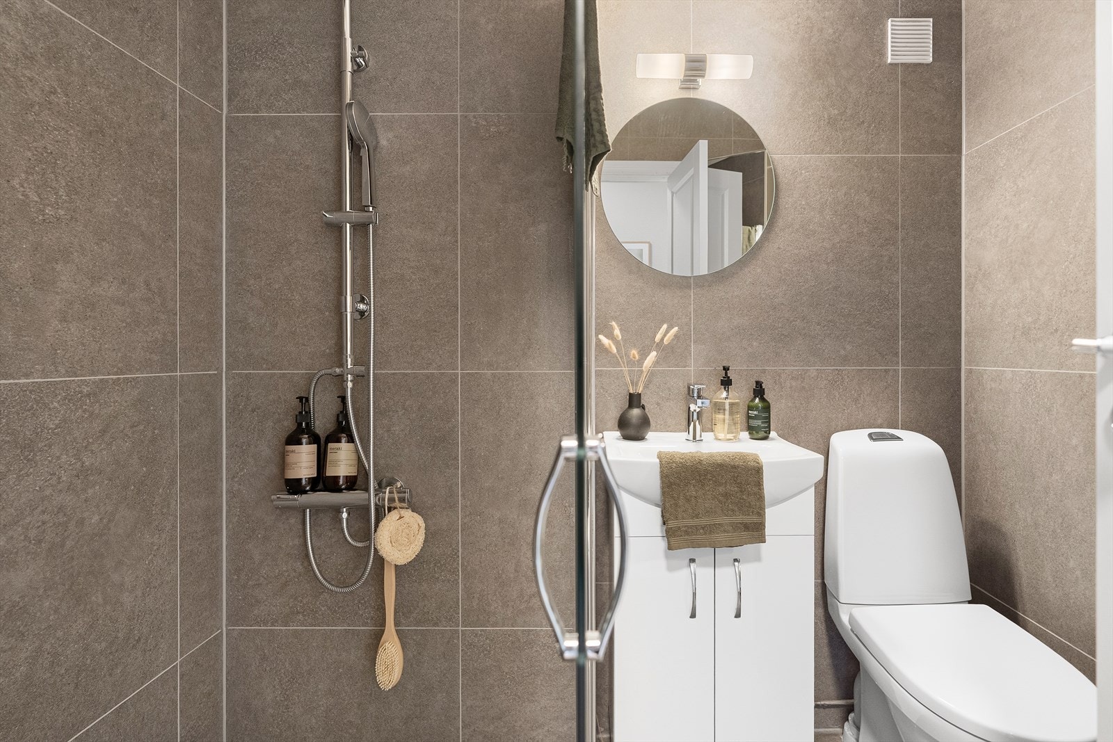 Badet inneholder toalett, helstøpt servant, skap under med slette fronter og dusjdører i klart glass Galleribilde