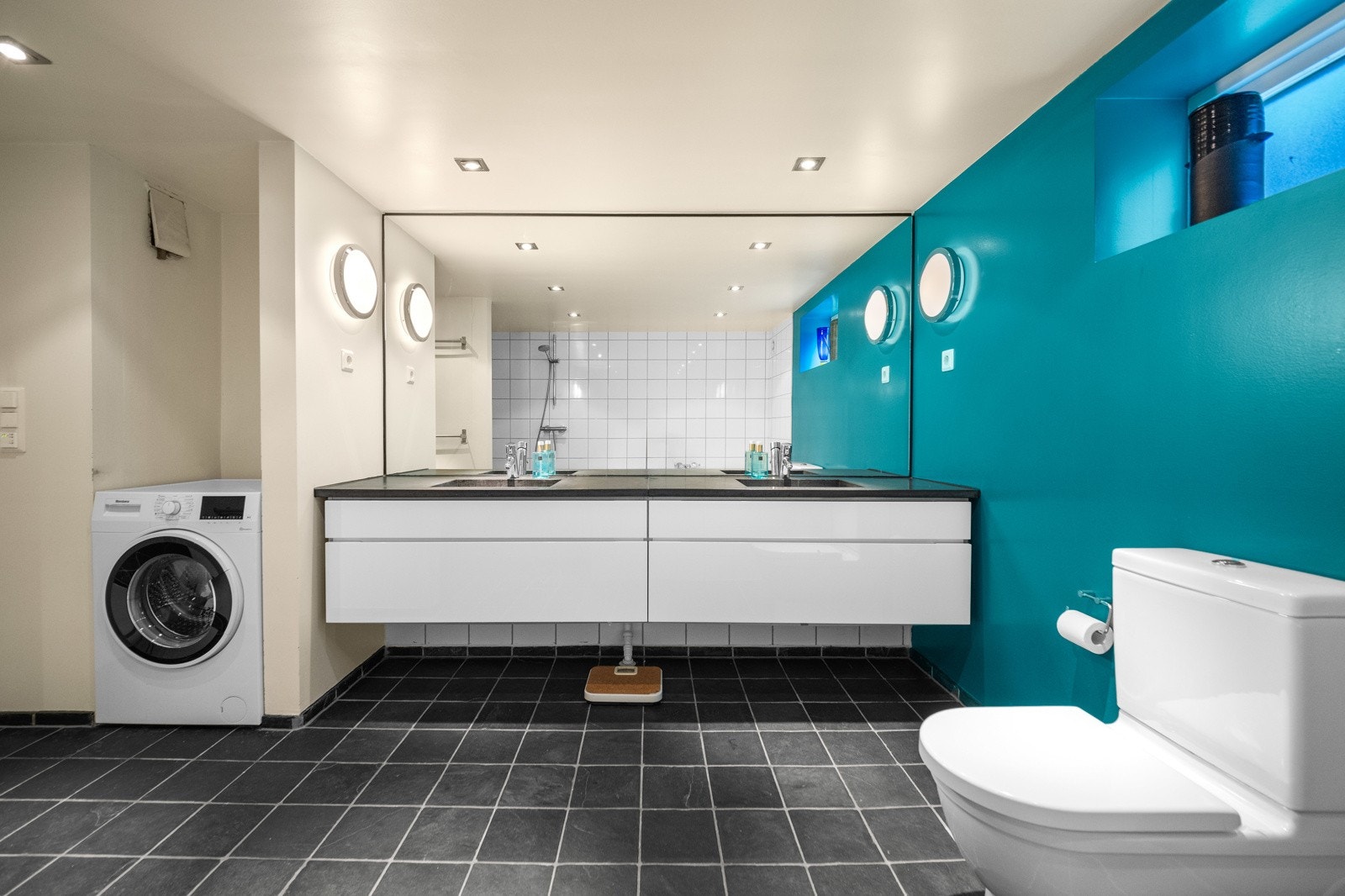 Delikat flislagt bad innredet med dusjnisje, dobbel baderomsinnredning med speil, gulvstående toalett, og badekar. Galleribilde