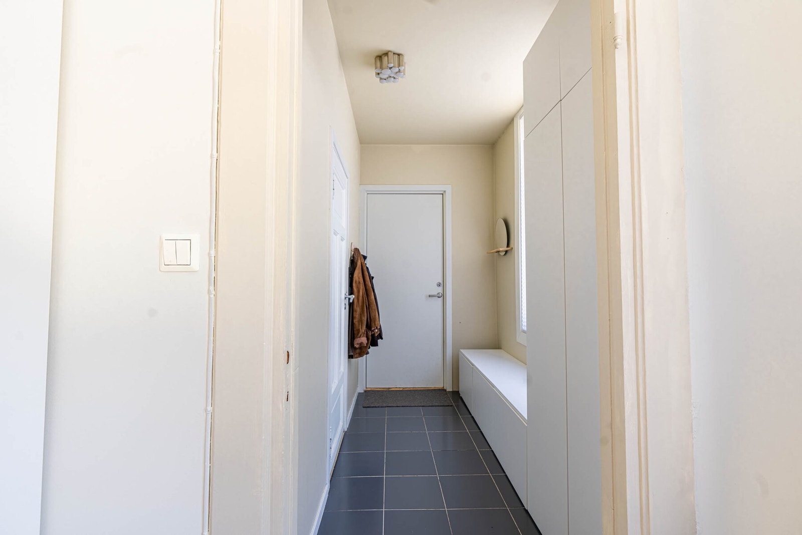 Flislagt entrè på 4 kvadratmeter med vegghengte knagger for yttertøy. Galleribilde