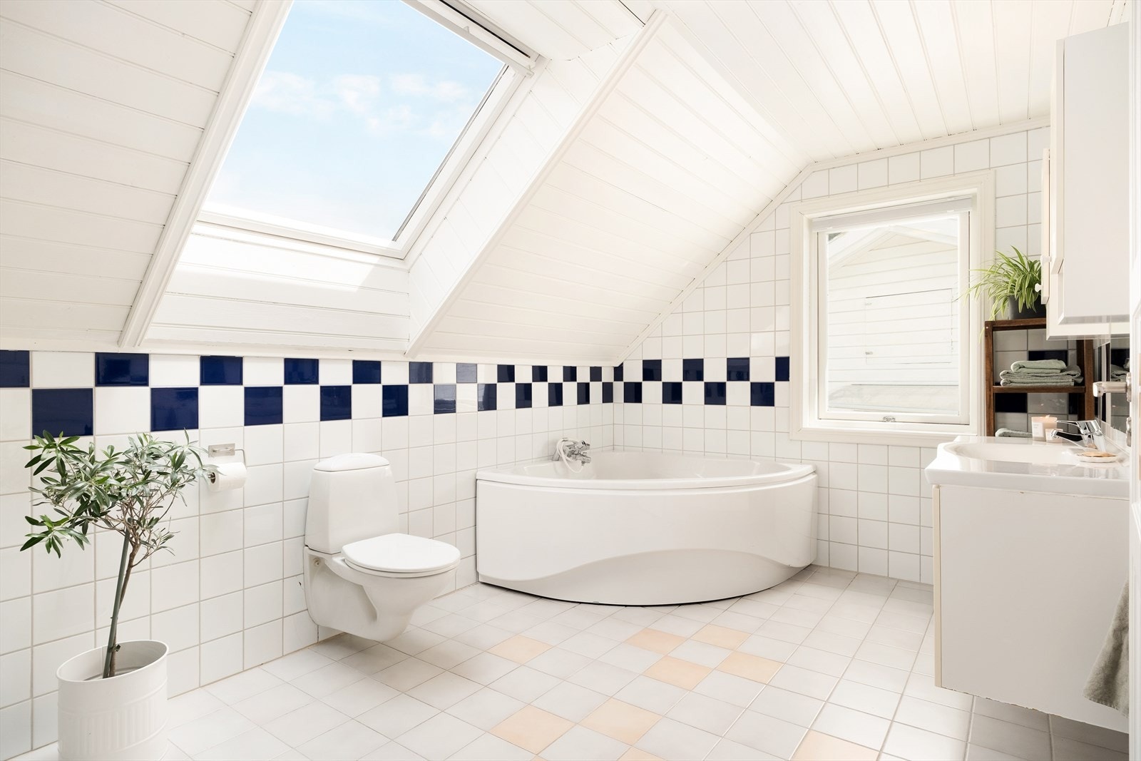 Badet er utstyrt med hjørnebadekar, dusjnise, baderomsinnreiing med benkeskåp, servant, overskåp, spegel og lyslist, vegghengt toalett og opplegg for vaskemaskin. Galleribilde