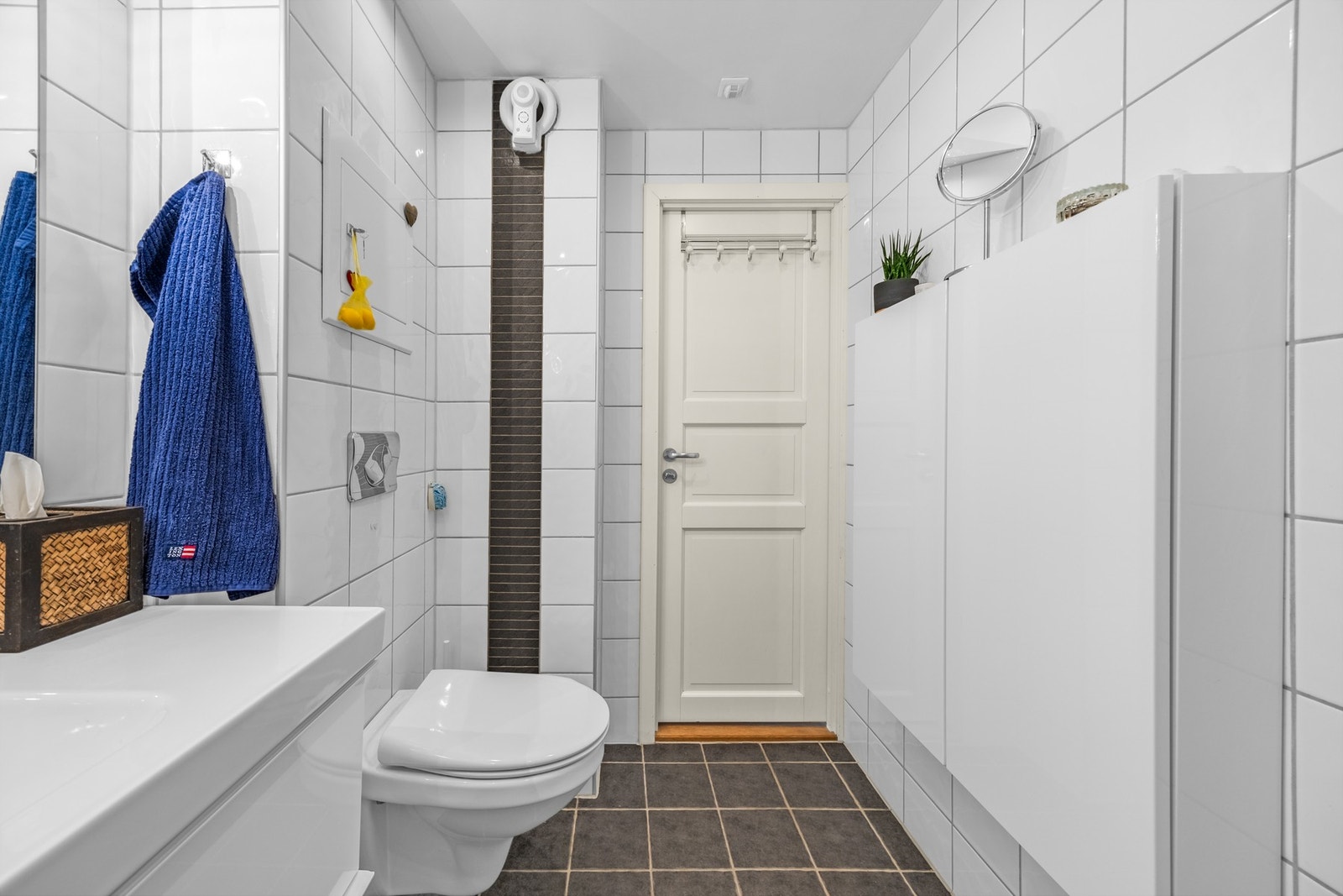 Videre er badet utstyrt med veggmontert klosett, heldekkende servant i skuffeseksjon og vegghengt skap med ekstra lagringsplass. Galleribilde