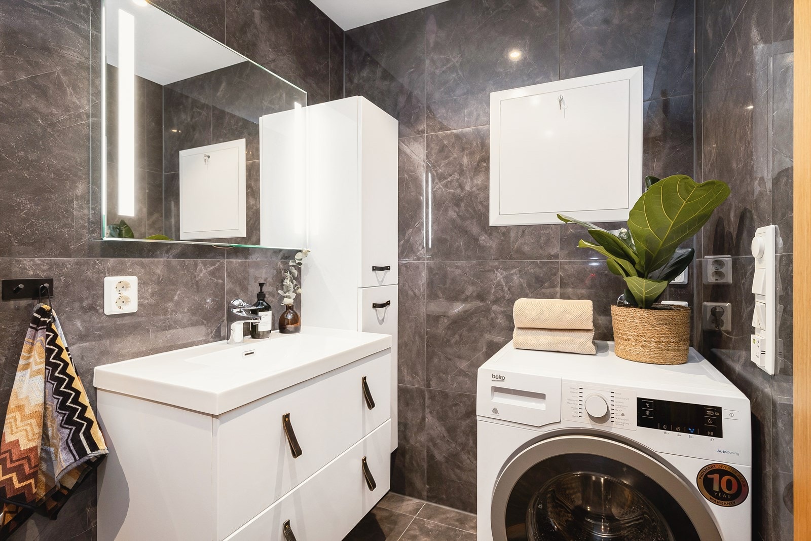 Badet inneholder vegghengt toalett, innredning med servant, opplegg for vaskemaskin, egen dusjsone og skap til lagring. Galleribilde