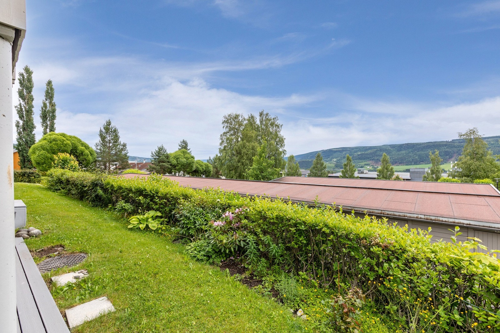 Utenfor plattingen er det en frodig hekk og plen. Galleribilde