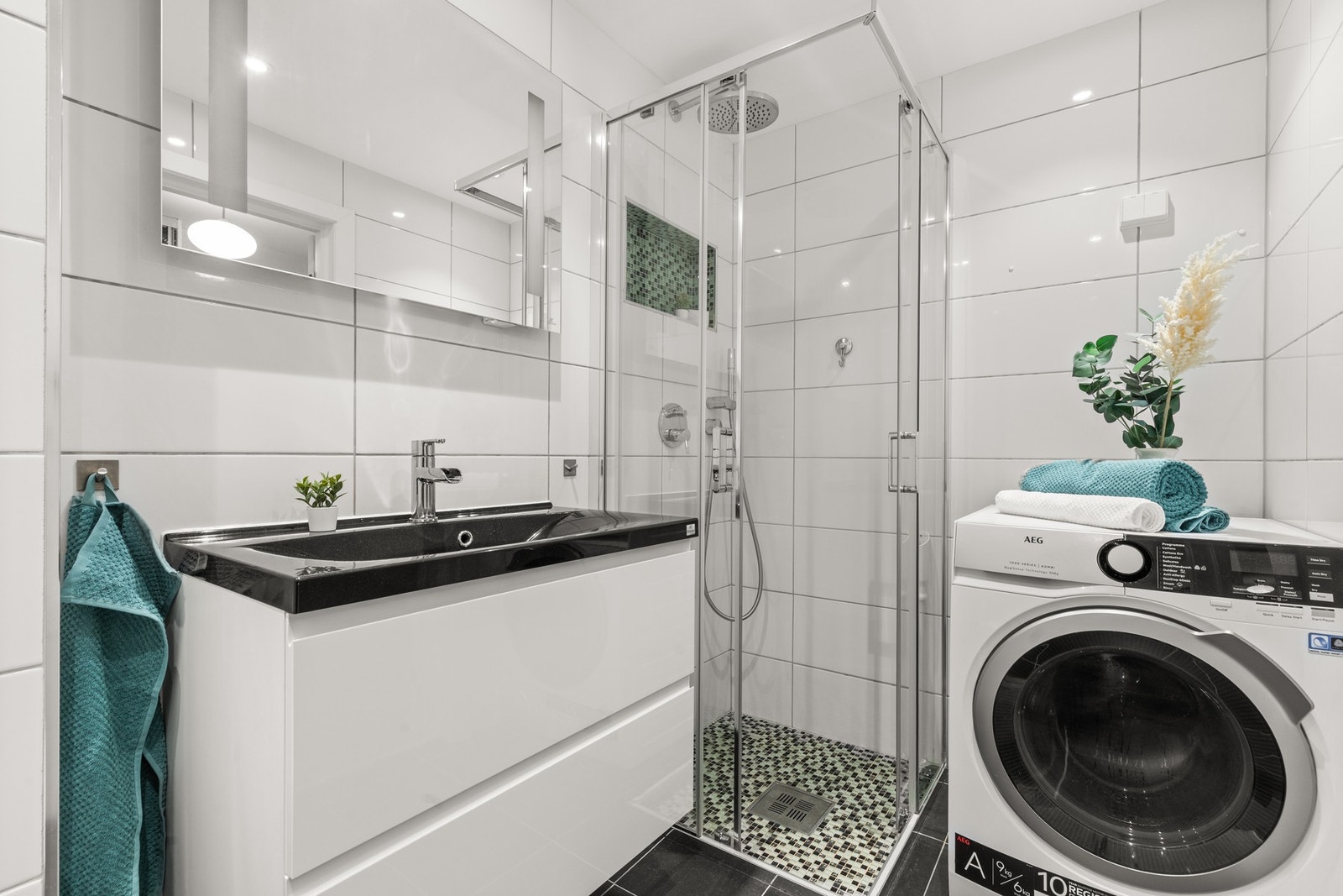 Lekkert flislagt baderom med dusj, servant, vegghengt wc, og opplegg for vaskemaskin. Galleribilde