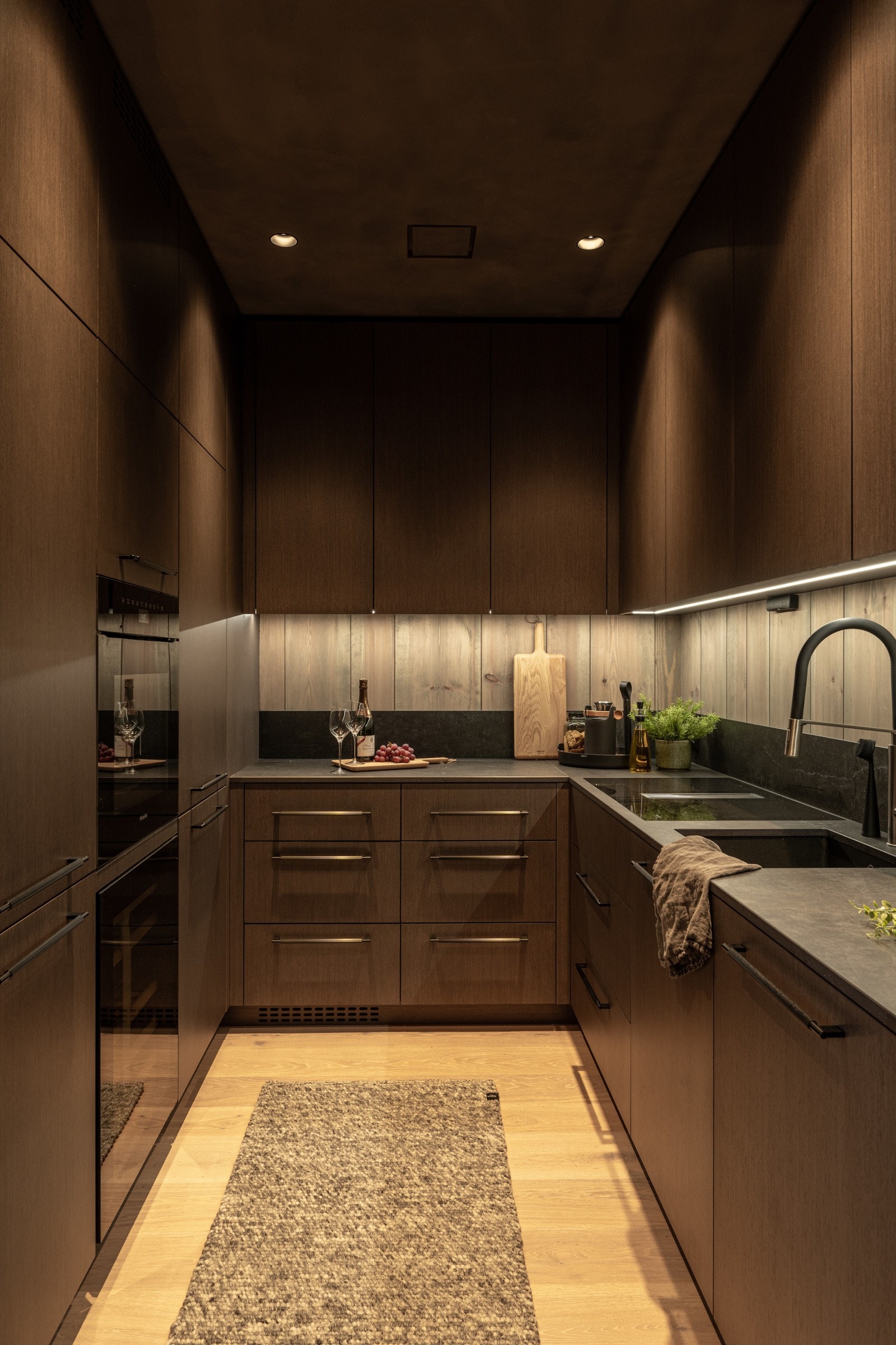 Den delikate og gjennomtenkte innredningen har fronter i grå eikefinér, sorte moderne håndtak og LED-belysning i skuffer og vitrineskap. Den naturtro grå benkeplaten fra Dekton har underlimt oppvaskkum og armatur i høy kvalitet. Galleribilde