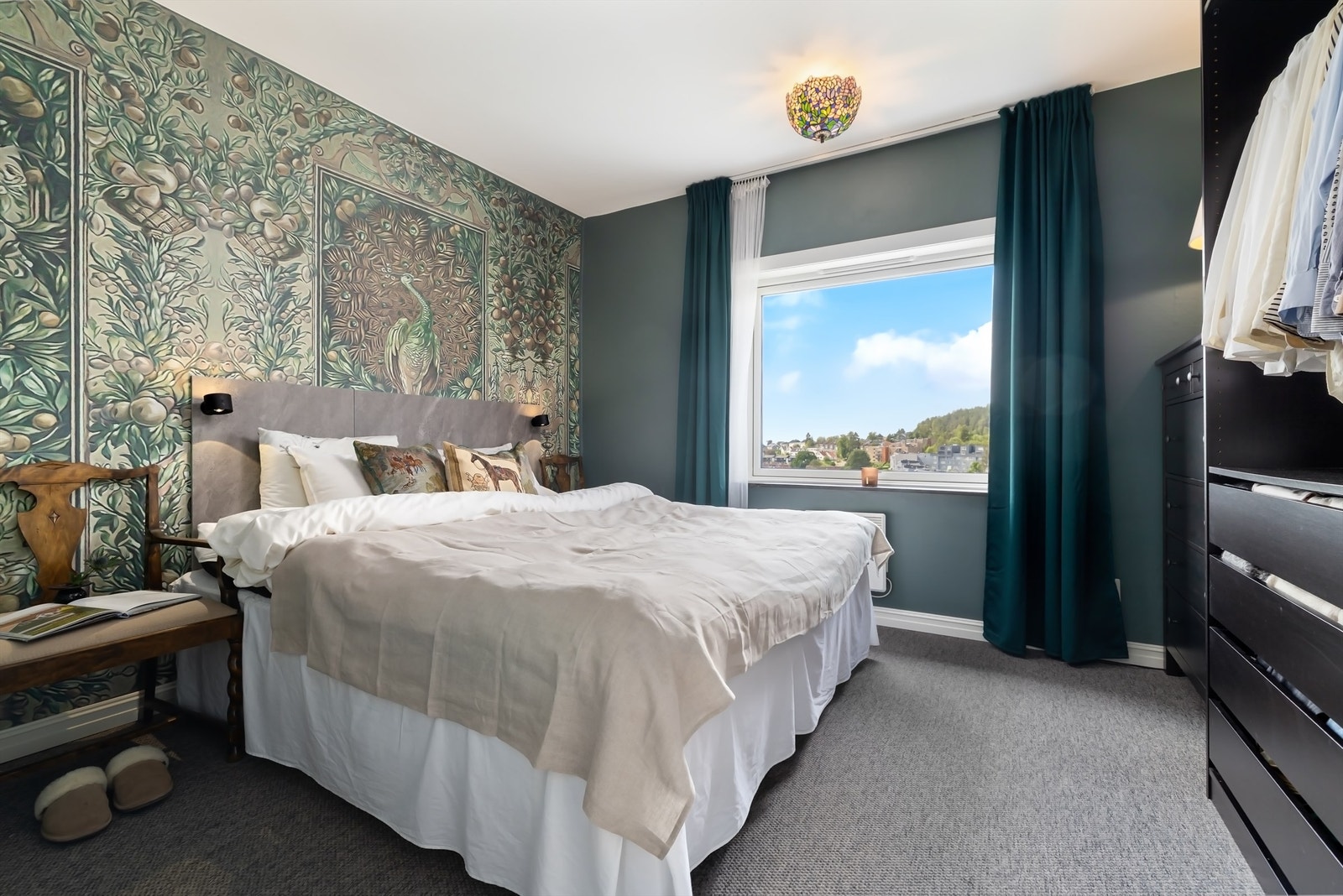 Veggflatene er malt i en lun farge med lekker, mønstret tapet på en vegg, på gulv er det lagt vegg-til-vegg teppe Galleribilde