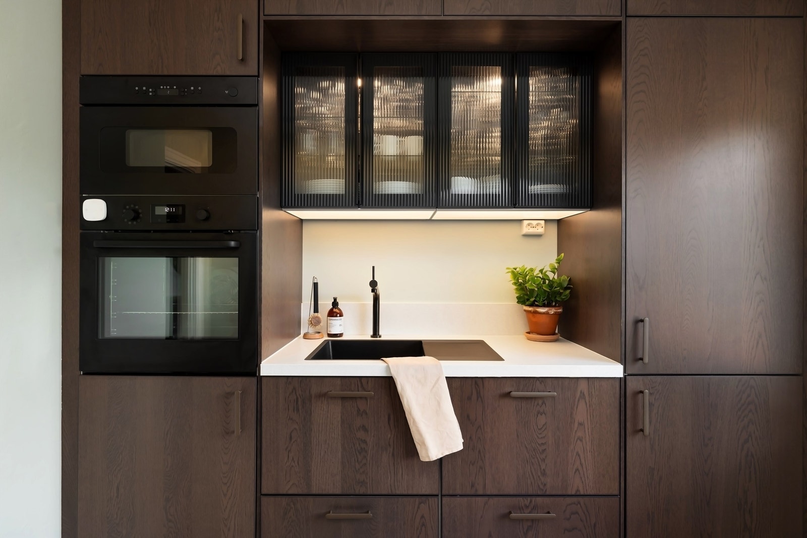 Integrerte hvitevarer som kjøleskap, oppvaskmaskin, stekeovn og mikrobølgeovn, samt koketopp med ventilator på vegg over Galleribilde