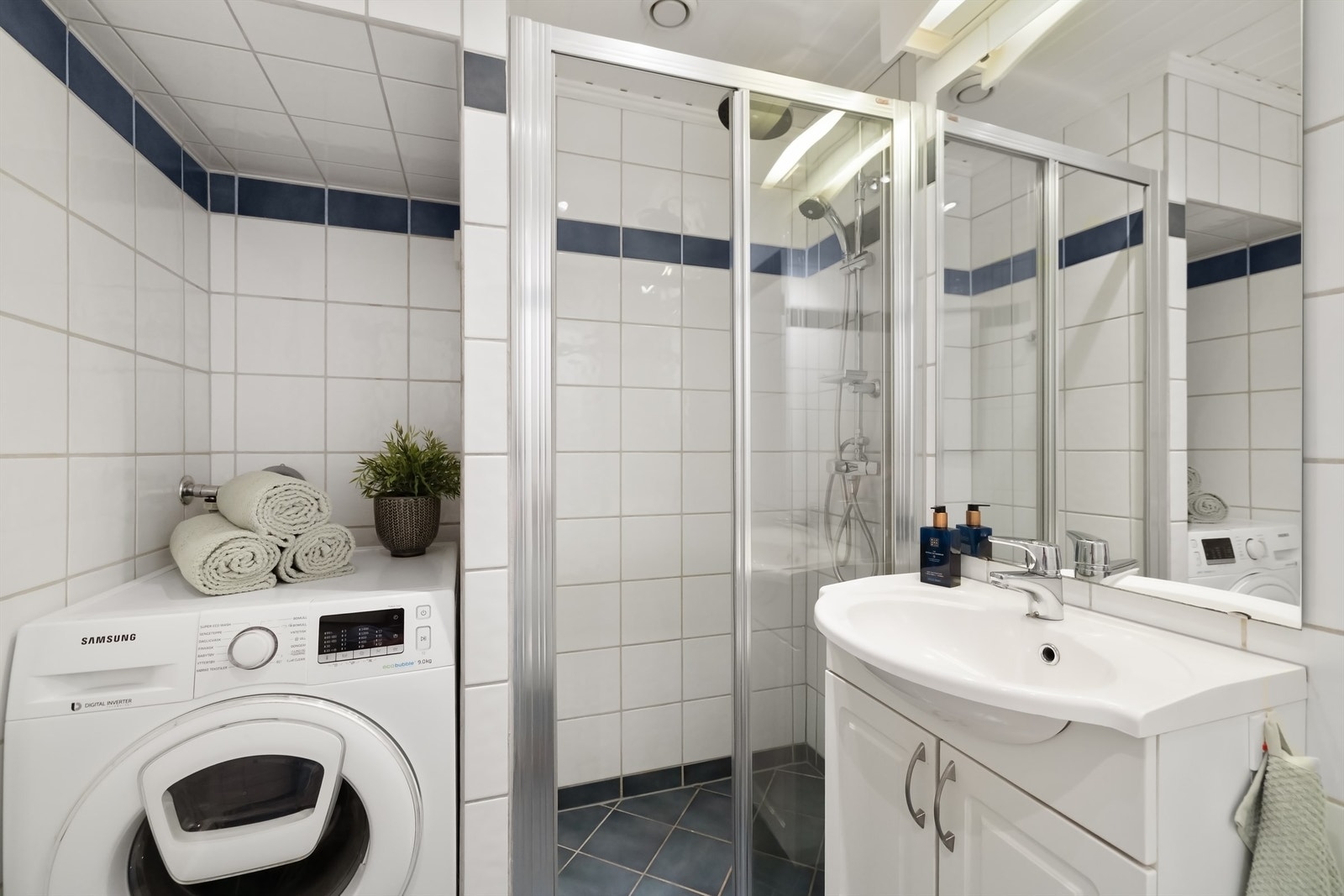 Lyst, flislagt baderom med gulvvarme utstyrt med vegghengt servantskap med lyse, profilerte fronter, heldekkende servant med ett-greps armatur og speil med overlys Galleribilde